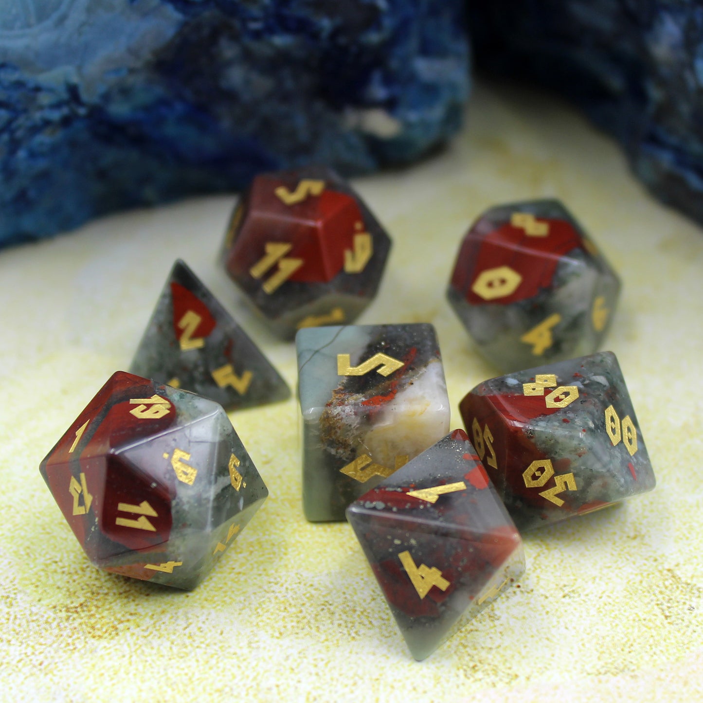 Full Bloodstone dice set displayed on a battlemap, featuring natural green and red gemstone dice with gold leaf numbering.