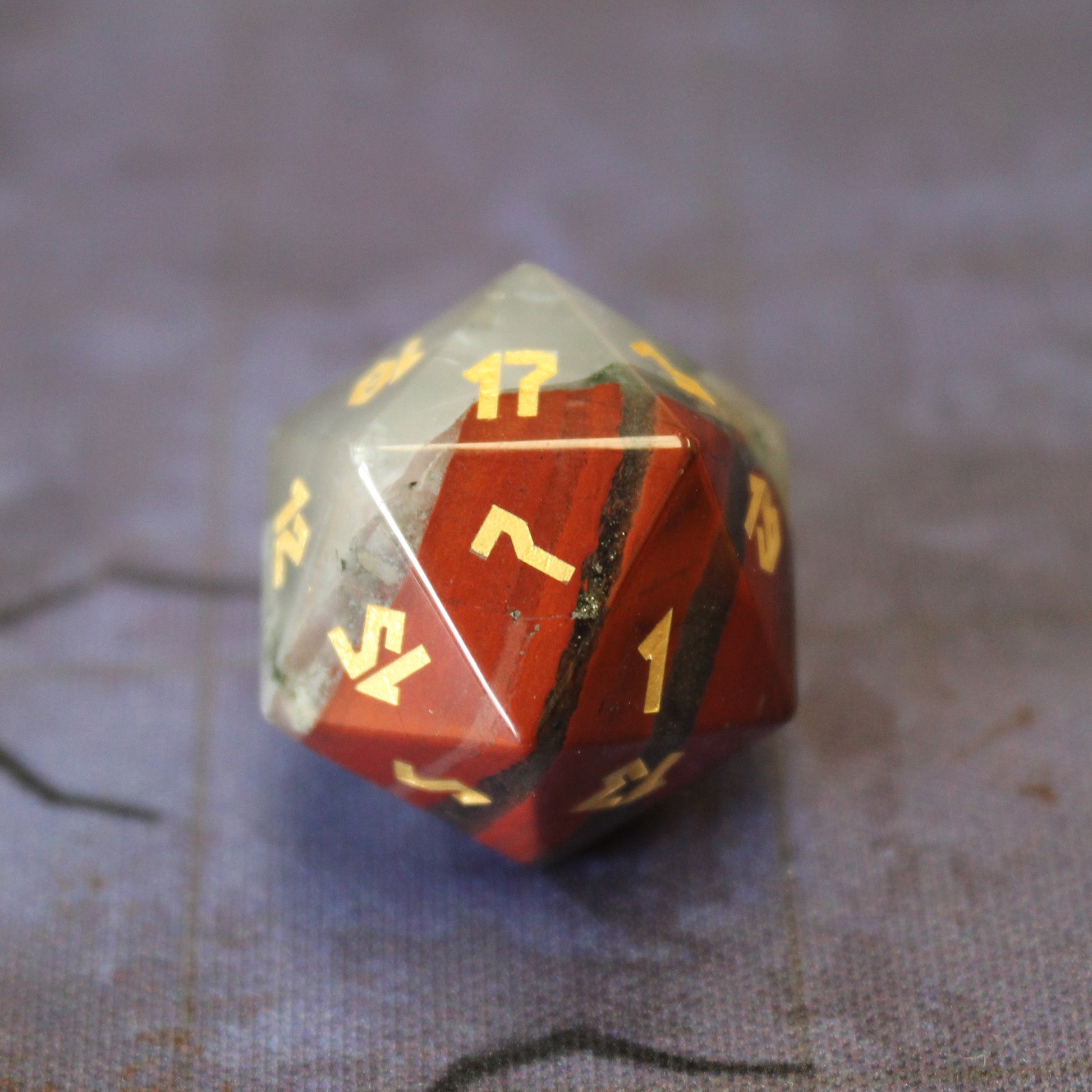Close-up of the Bloodstone D20 with red hematite spots and gold leaf numbering.