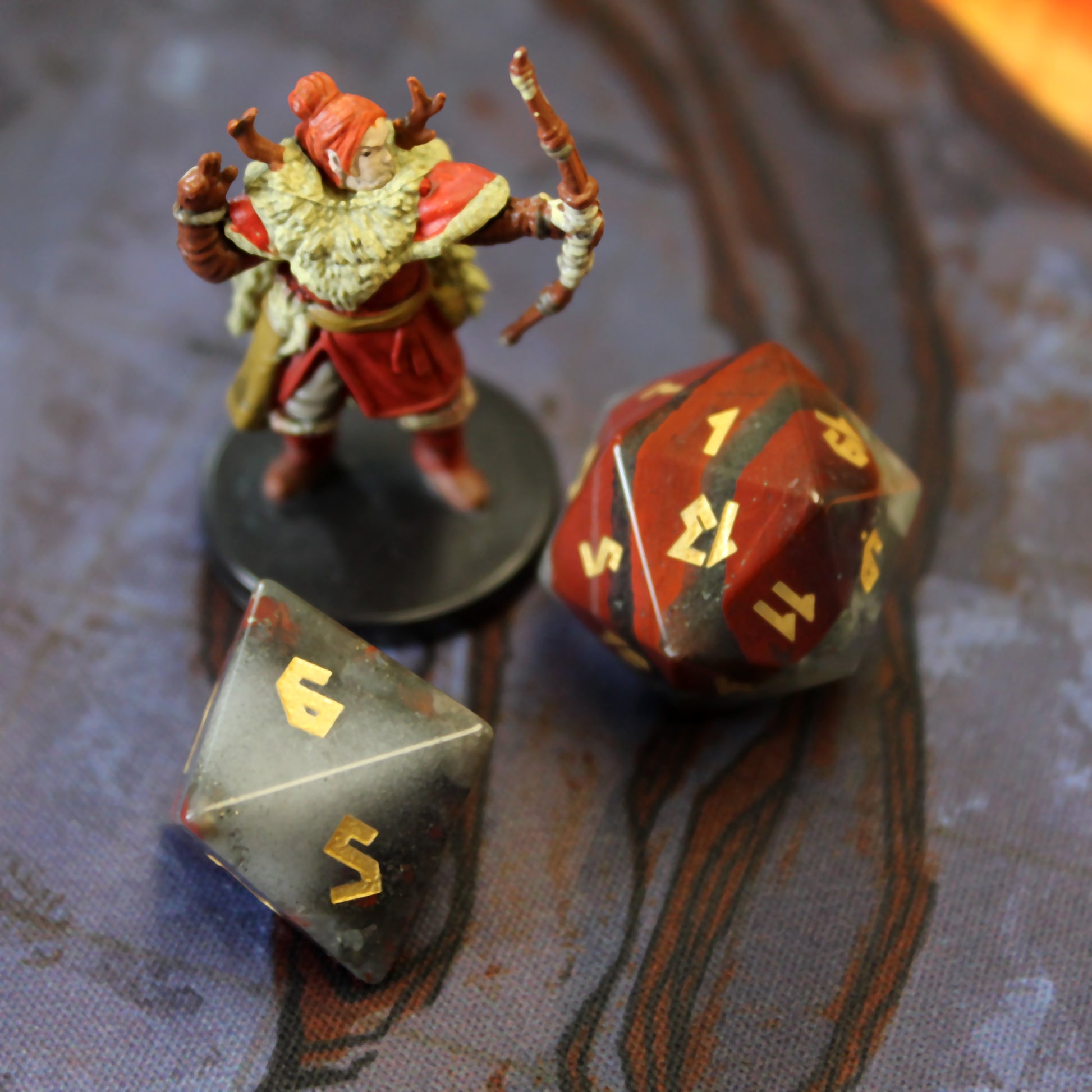 Close-up of the full Bloodstone dice set, highlighting vibrant red hematite spots and intricate gold leaf numbering on the green chalcedony dice.