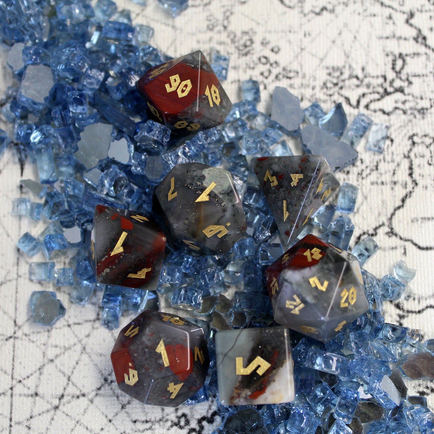 Bloodstone dice set spread out on an old map, featuring deep green chalcedony with red hematite spots and gold leaf numbering.