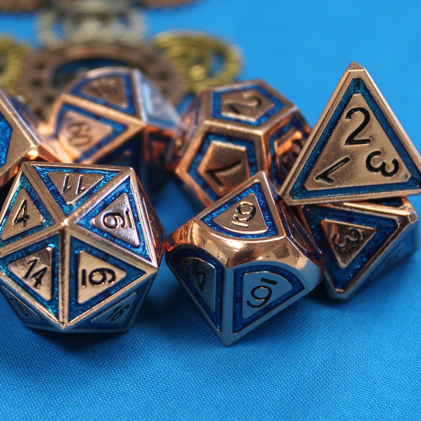 Full metal BullsEye Blue tabletop gaming dice set resting on a blue cloth surface with a closeup view of the d20, d10 and d4 showcasing the semi-transparent enamel border of the BullsEye line.