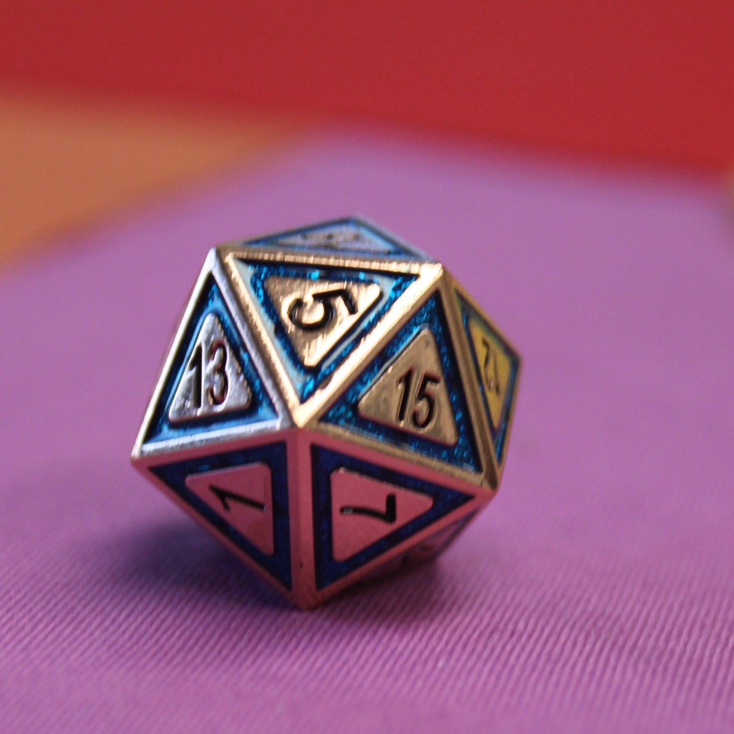 Closeup image of the d20 from the Metal BullsEye Blue dice set on a purple background.  The 5 face is towards the viewer and the lighting shows the recessed UV hardened enamel surrounding the numbering.