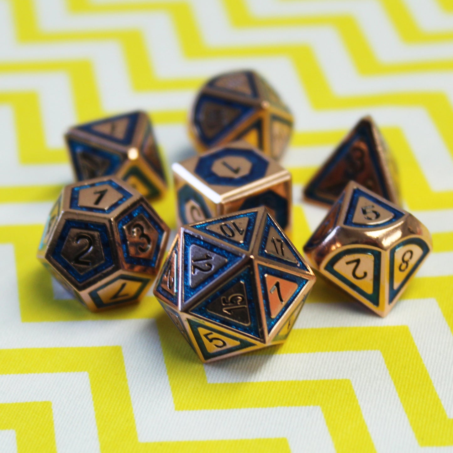 Dice Dungeons' metal BullsEye Blue dice set on a yellow and white zigzag surface with the d20 towards the viewer showing the 10 face.  The dice are copper in color with a blue inset and black numbering.