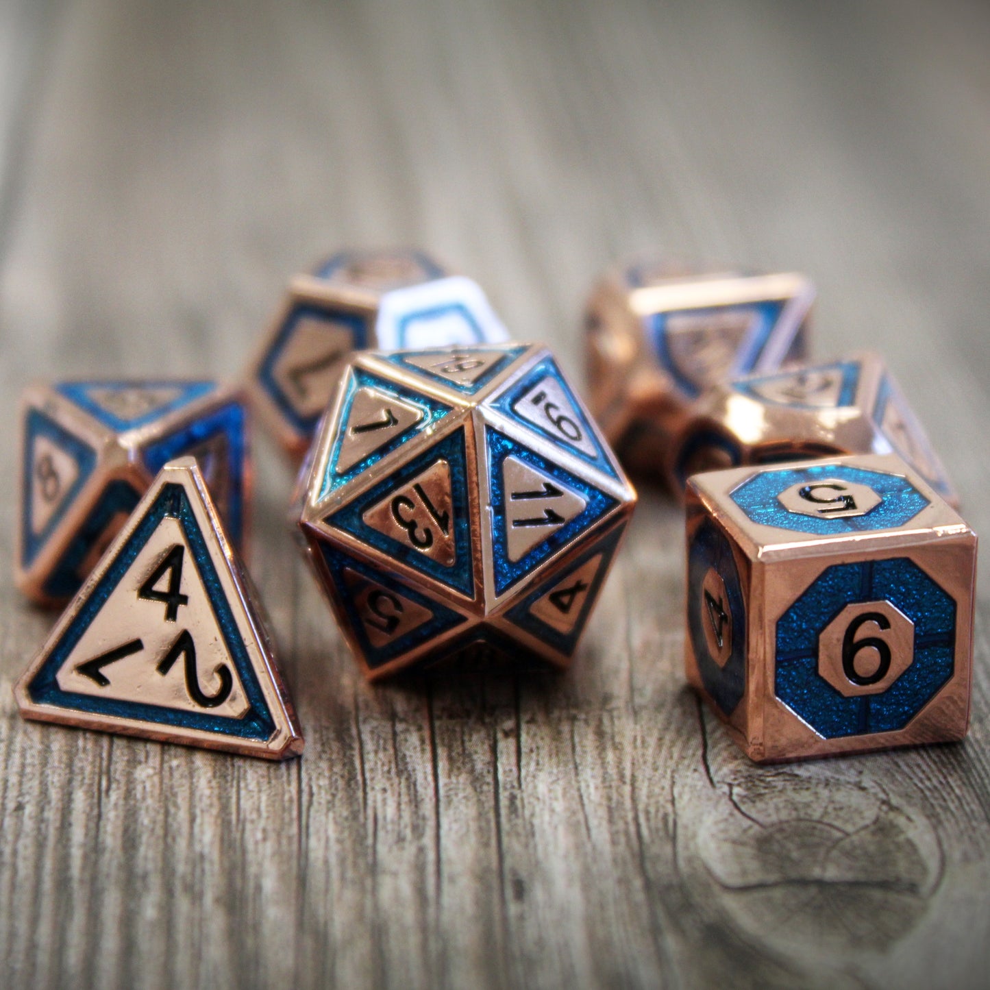 Copper & Blue Tabletop RPG Dice set BullsEye Blue resting on a wooden surface with the d4, d20, and d6 forward.  With high contrast of black ink on copper, this set offers high readability.