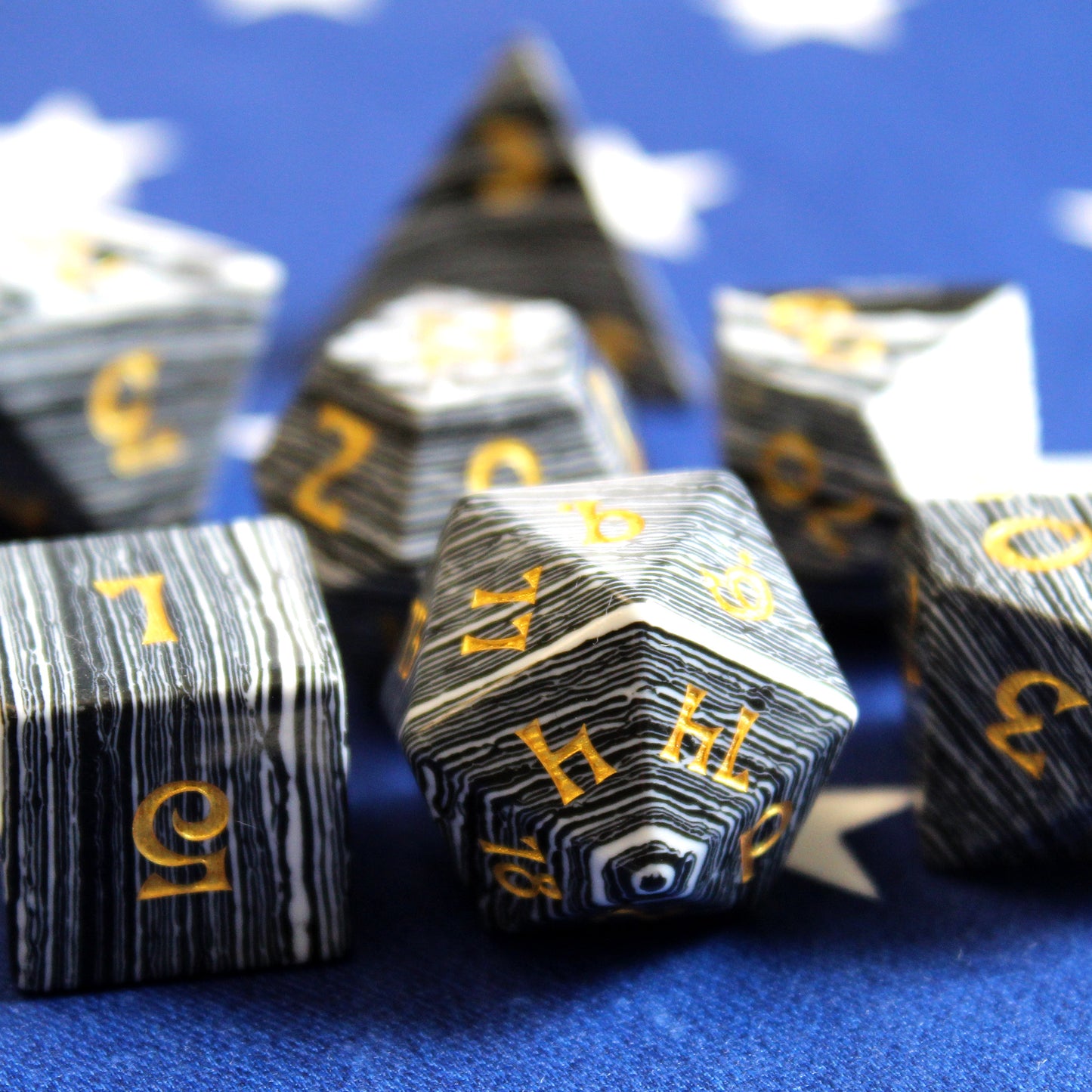 Close Up of Set of Black and White Striped Dice with Gold Numbering on a Blue Fabric Background