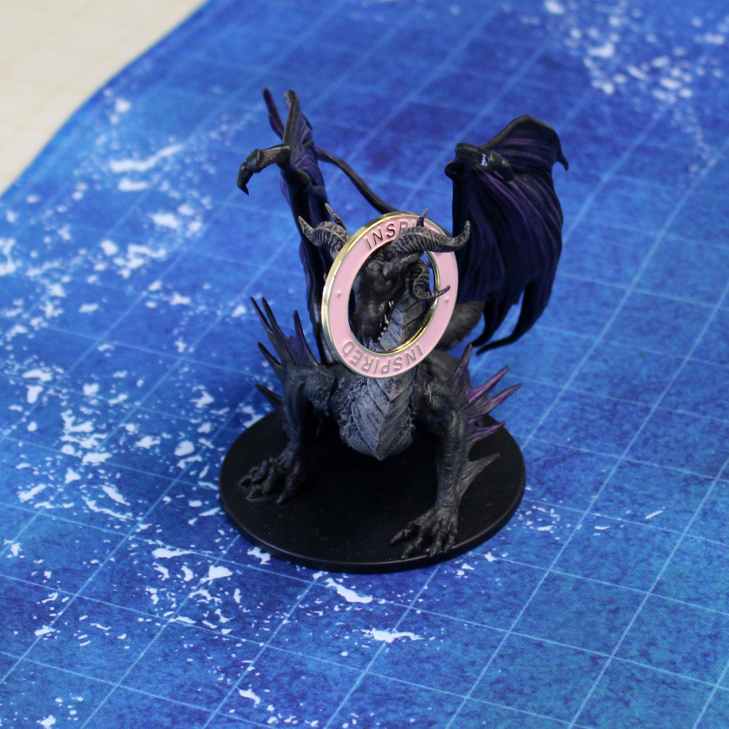 Gold and pink Inspired condition ring placed on a black dragon miniature, marking the character's inspiration effect in a tabletop RPG session.