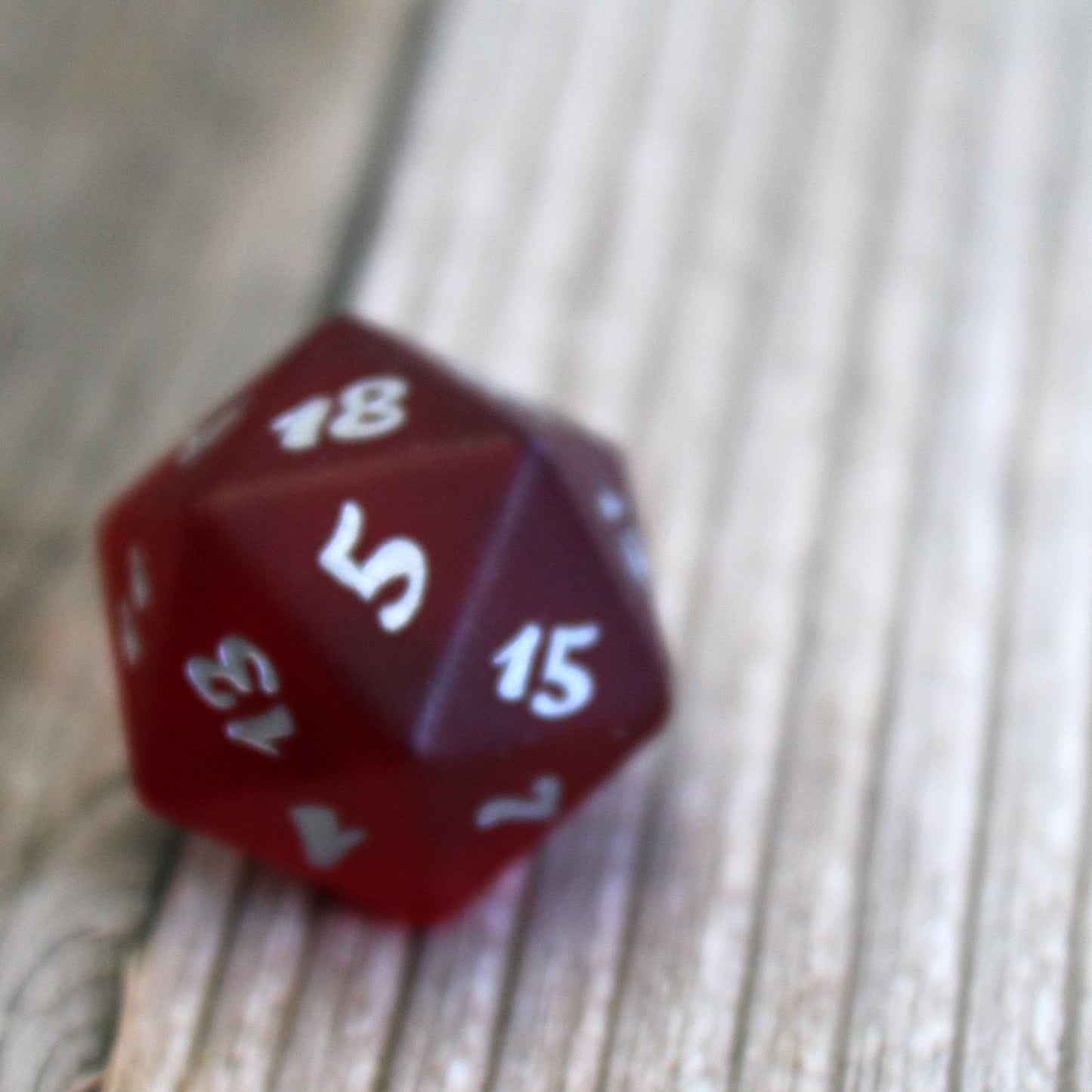 A single red translucent glass twenty-sided die with silver numbering on a wooden surface.