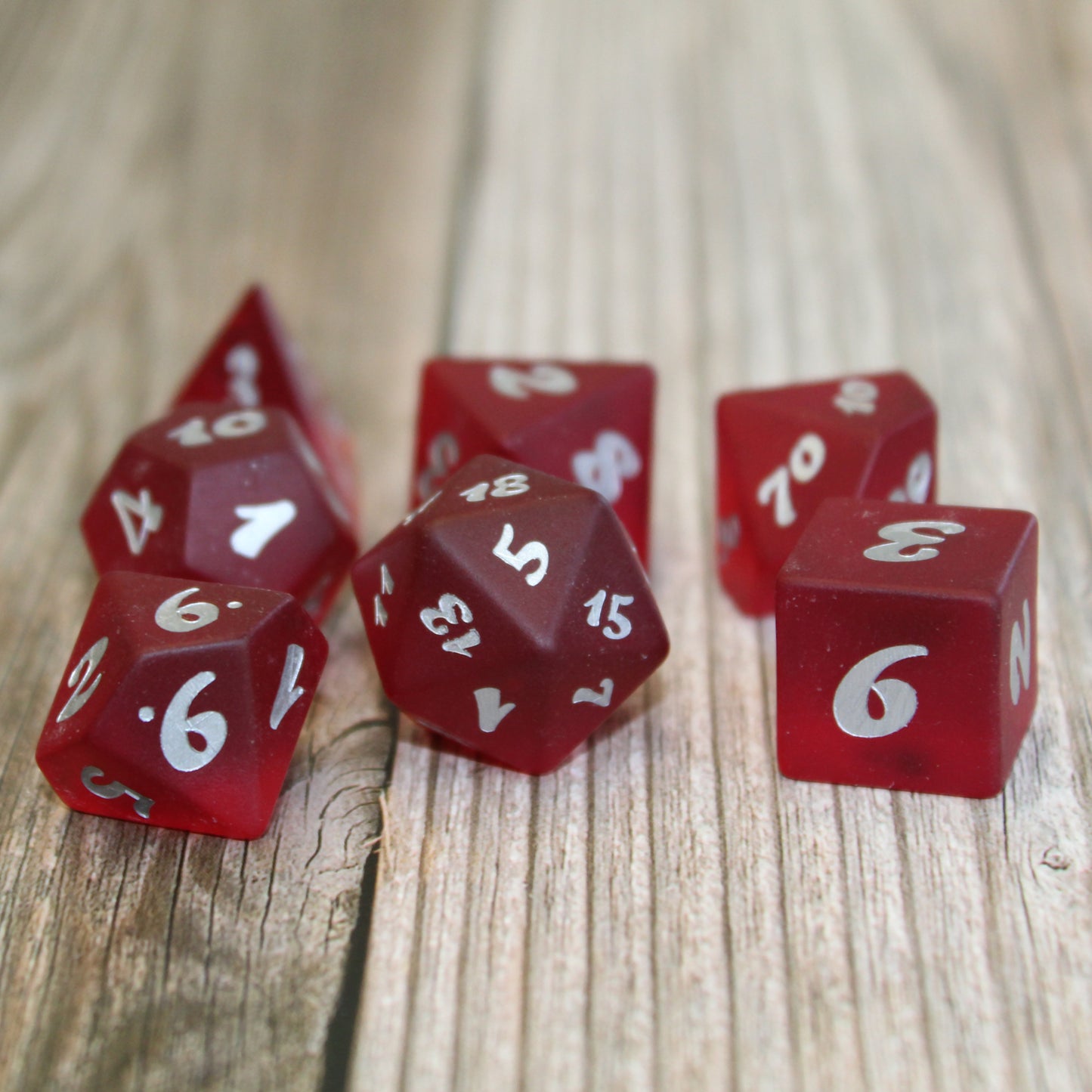 A set of red translucent glass RPG dice with silver numbering on a wooden surface.