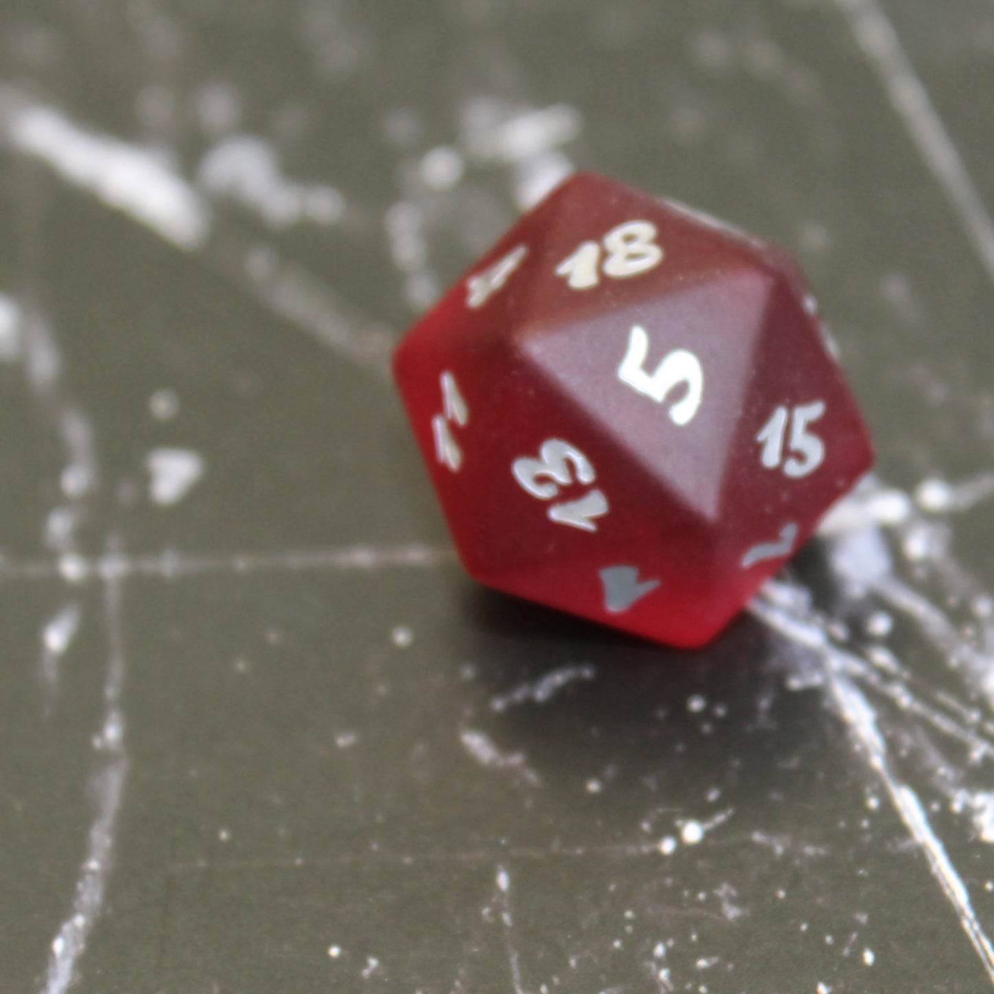 Closeup of a red translucent glass twenty-sided die with silver numbering on a black marbled surface.