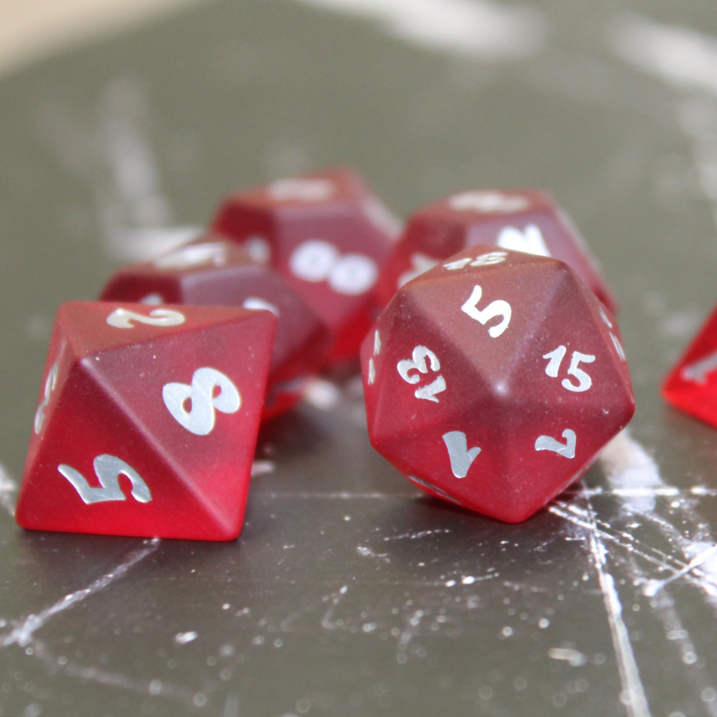 A photo of some red translucent glass RPG dice with silver numbering on a black marbled surface.