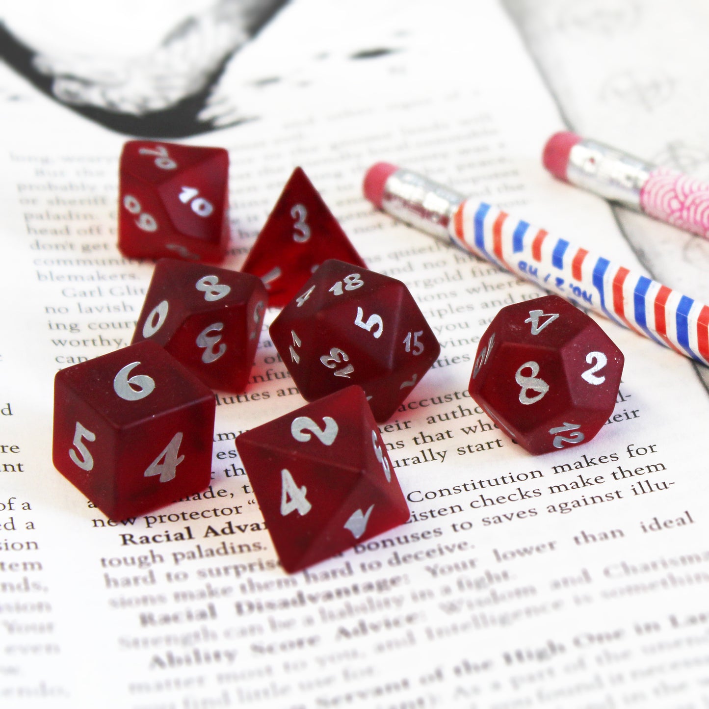 A set of red translucent glass RPG dice with silver numbering resting on the page of a book.