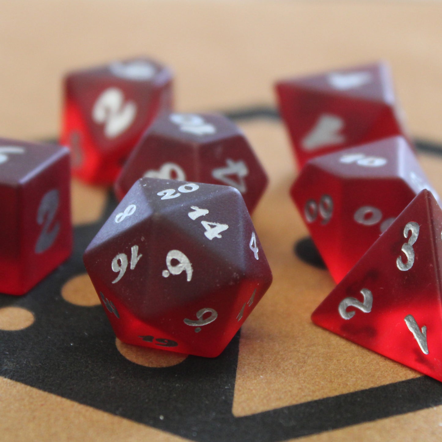 A closeup of a set of red translucent glass RPG dice with silver numbering sitting on a dice tray