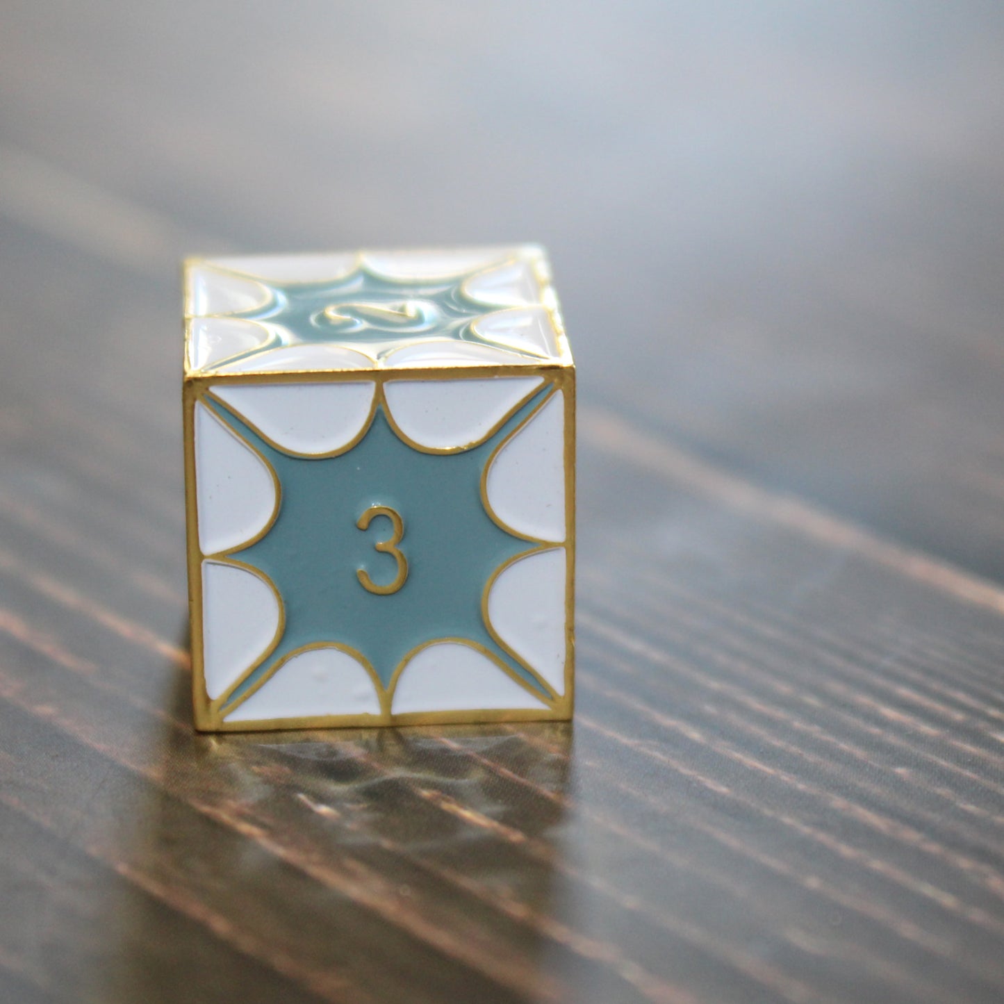 D6 die from the Metal DragonScale White Dice Set on a wooden table for RPG enthusiasts.