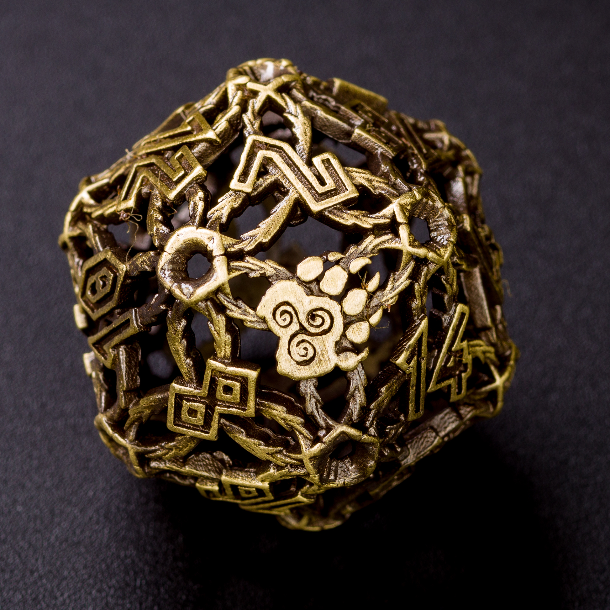 Closeup of a single bronze druid-inspired hollow metal twenty-sided die with uninked numbers and a glyph-covered paw in place of the high number on a black background