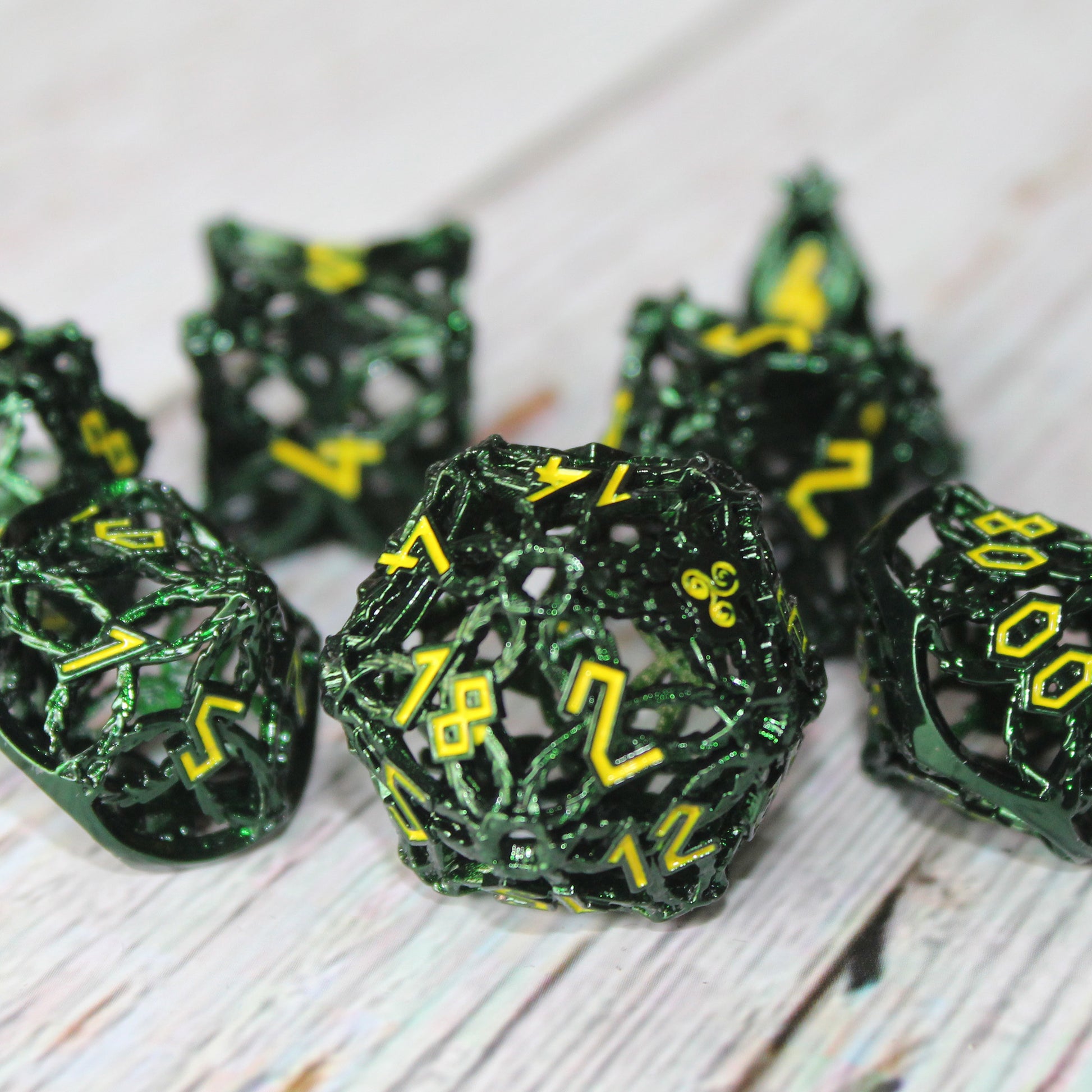 Closeup of a set of hunter green druid-inspired hollow metal RPG dice with yellow numbers and a glyph-covered paw in place of the high number on a gray wooden background