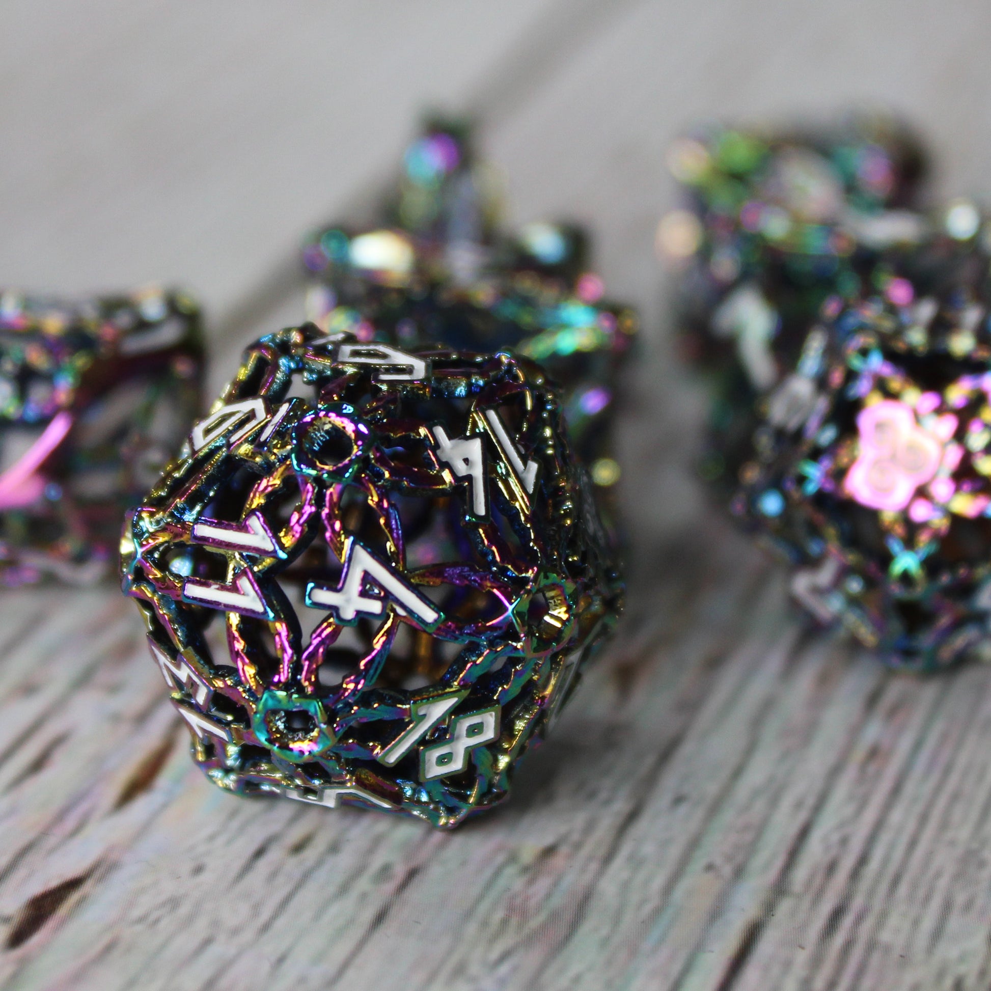 Closeup of a set of multicolored druid-inspired hollow metal RPG dice with white numbers and a glyph-covered paw in place of the high number on a gray wooden background