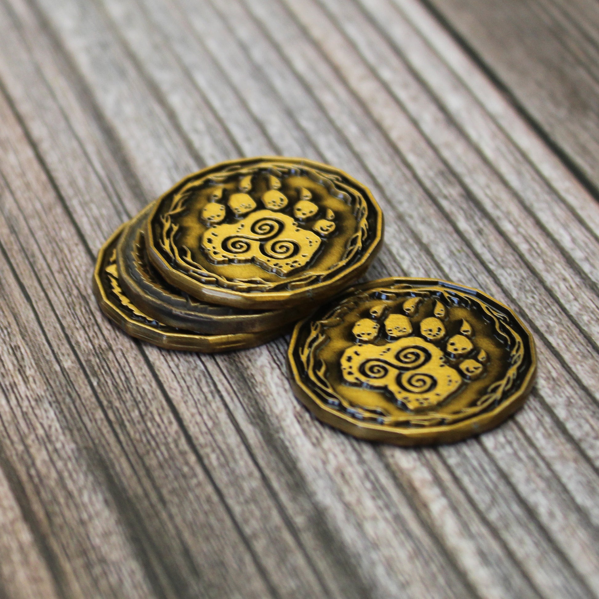Four gold druid character tokens arranged in a stack of three and one token next to them on a wooden surface. All visible token surfaces are on the "heads" side depicting a paw with triple spiral.