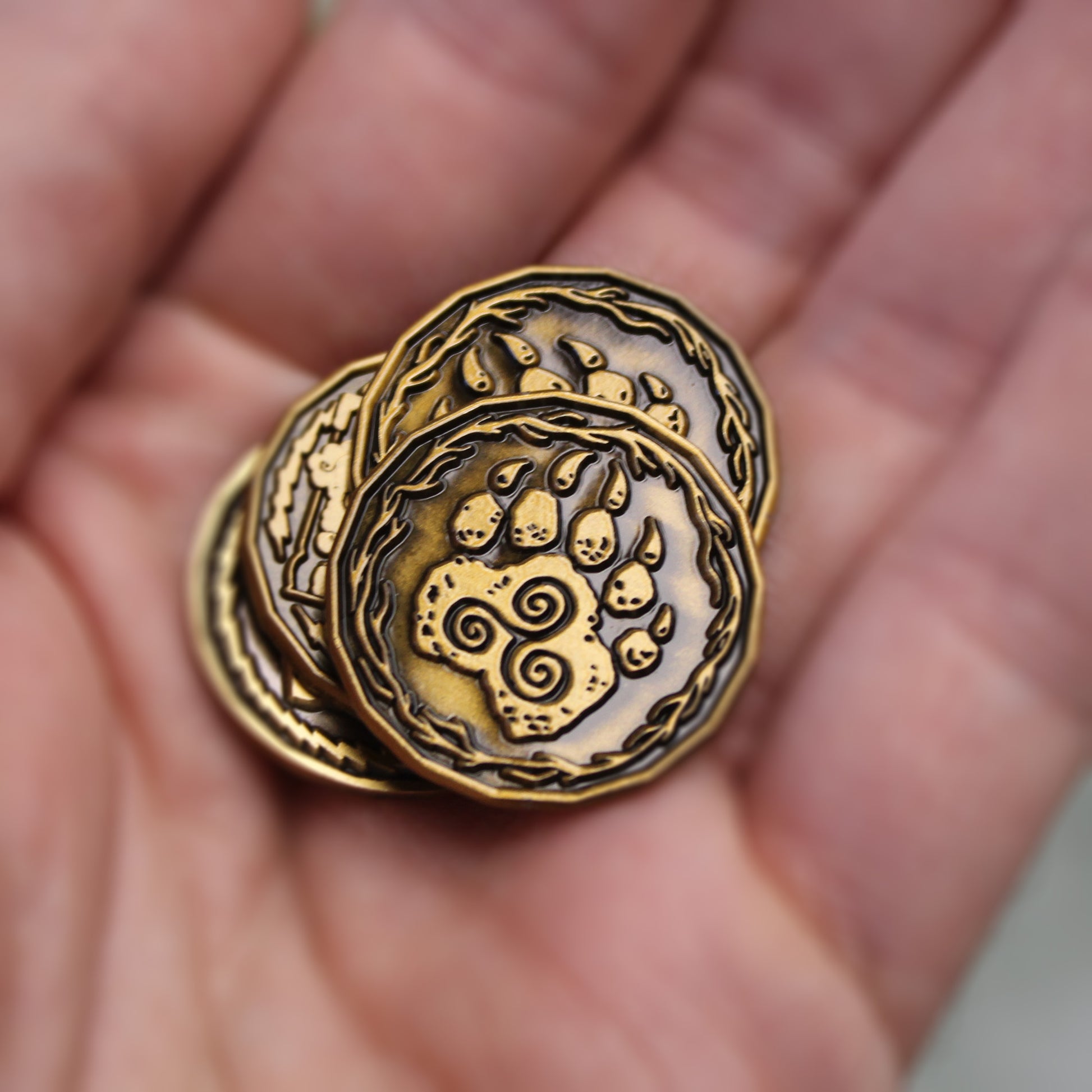 A stack of four gold druid character tokens in the palm of someone's hand. The top token is on the "heads" side, depicting a paw with a triple spiral.