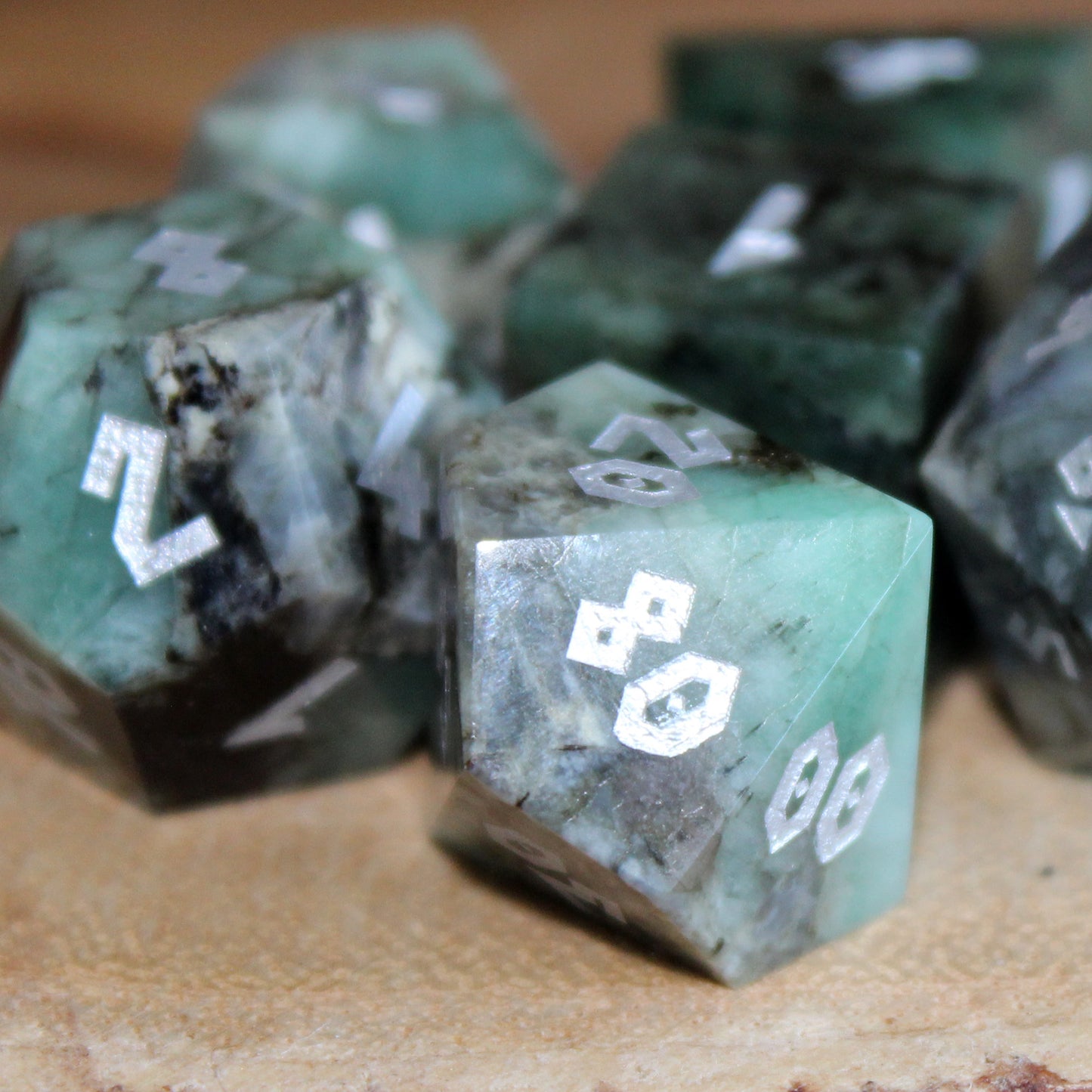 Raw Emerald dice set on a wooden table, with a close-up of the D100, featuring shimmering green stone and silver numbering, perfect for tabletop RPGs.