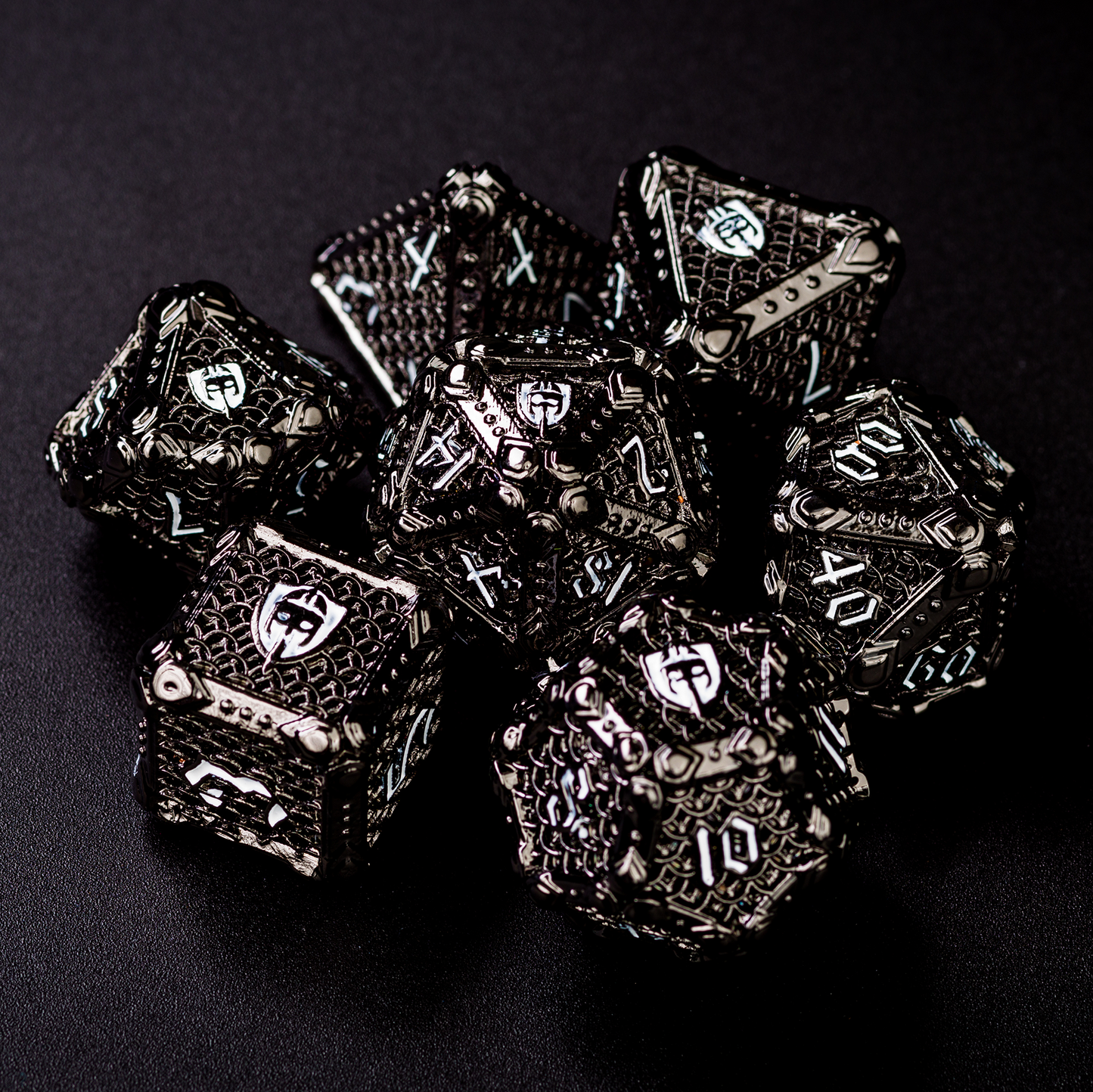 Set of black fighter-inspired hollow metal RPG dice with a chain mail background on each die face, white numbers, and a helmet, sword, and shield replacing the high number on each die on a black surface