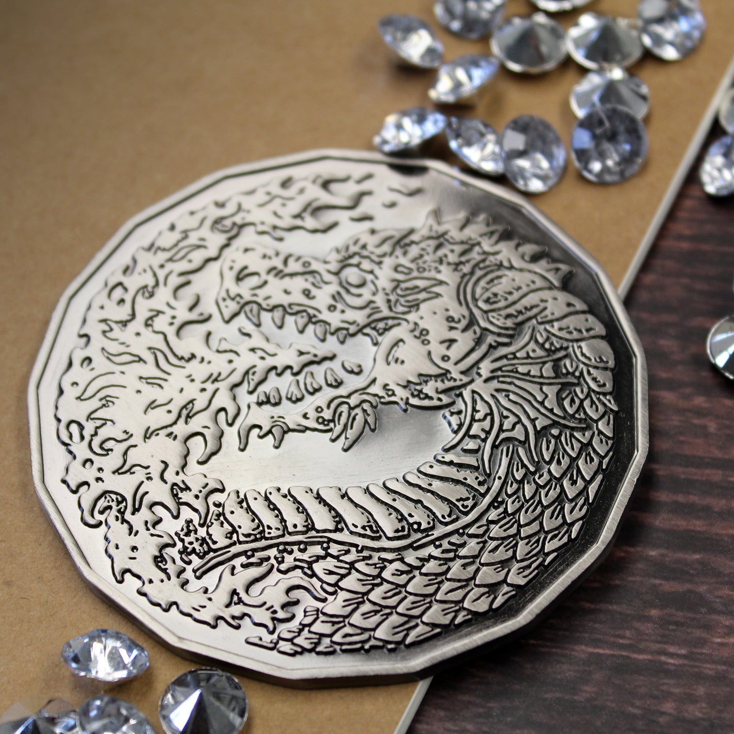 Adult Fire Dragon monster token on a wooden table. The antique silver coin is face side up, showing a fire breathing dragon.