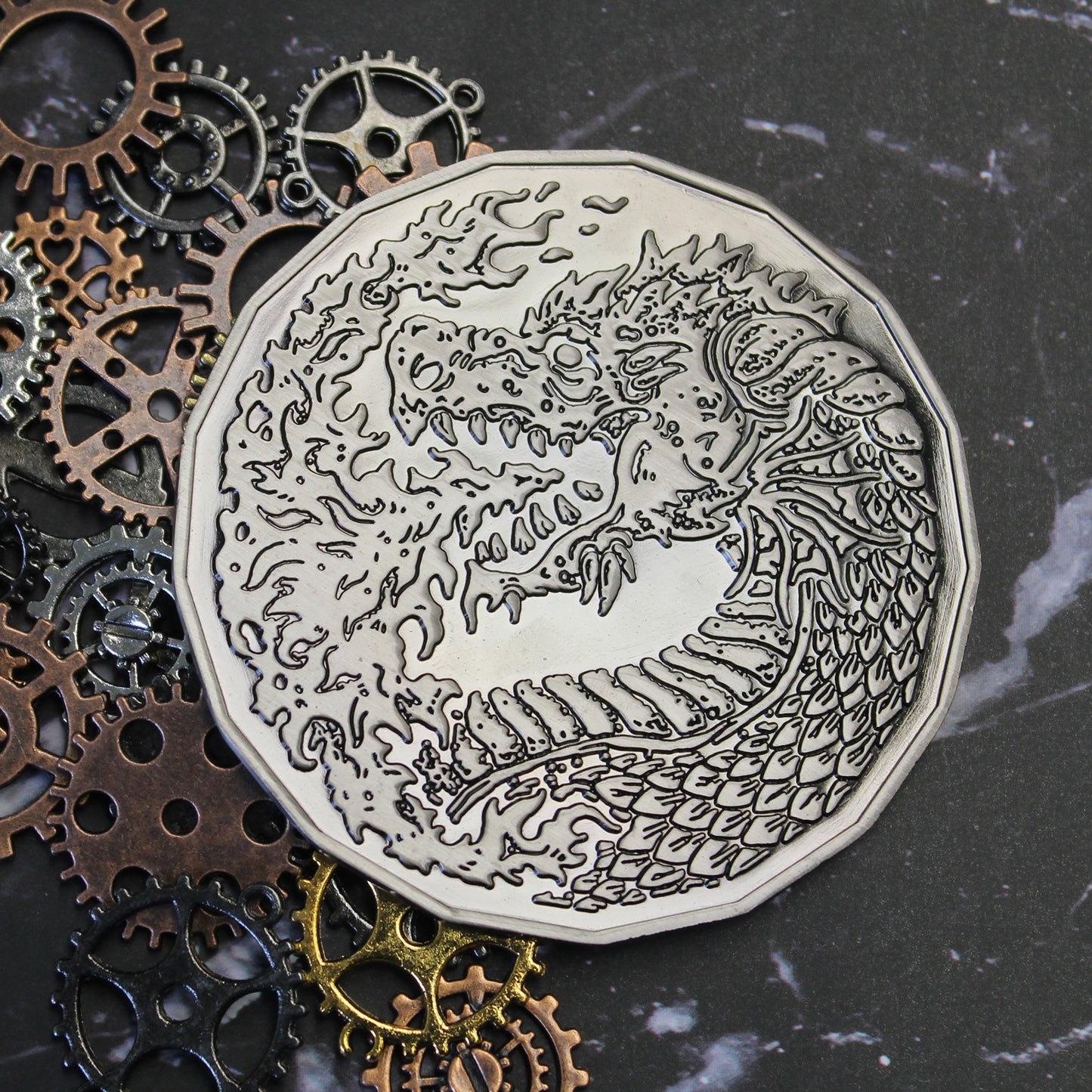 Adult Fire Dragon monster token resting on a black marble background with gears behind it, showing the engraved dragon breathing fire.