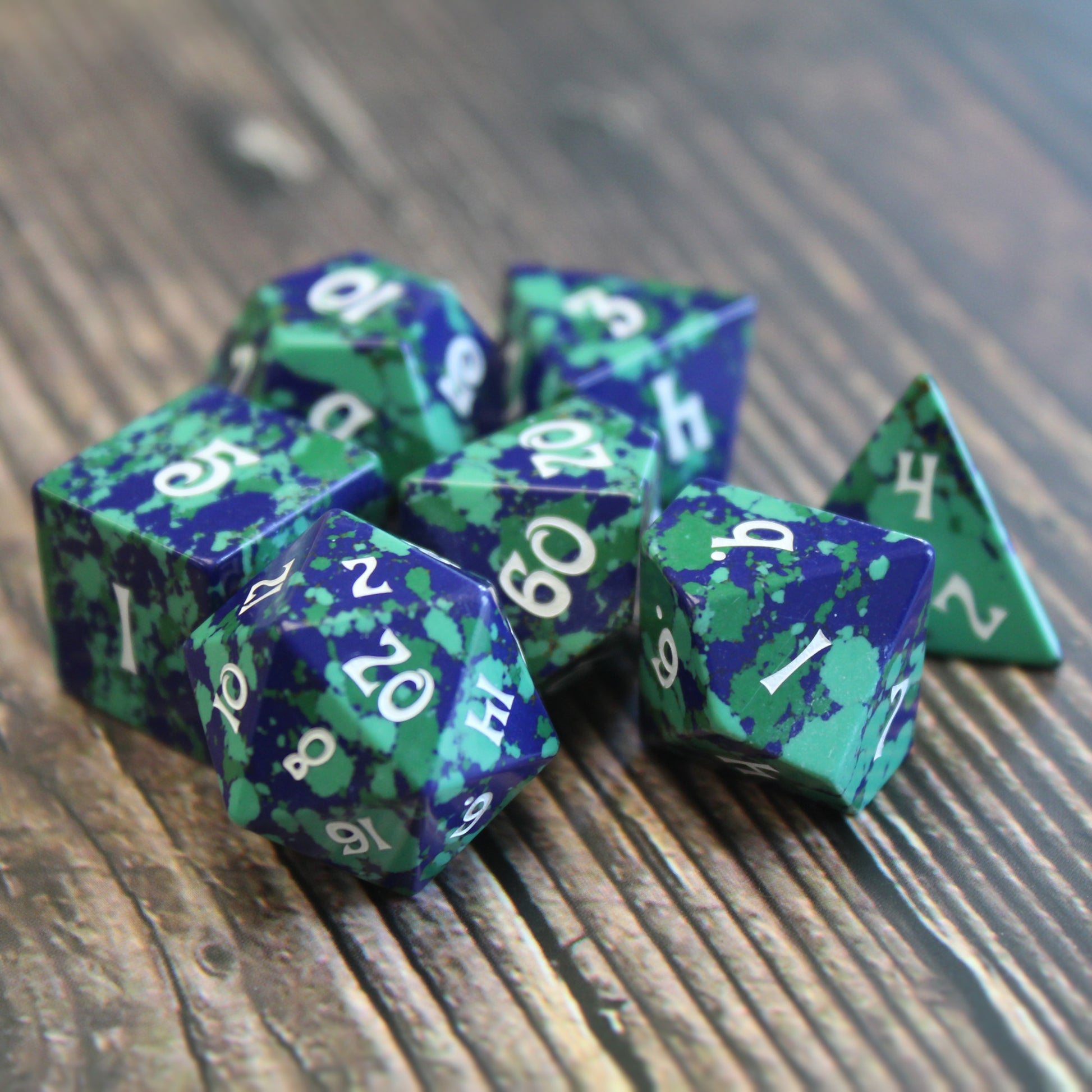 Gaia Groovy Stone Dice Set displayed on a table, featuring deep greens and blues ideal for DnD gameplay.
