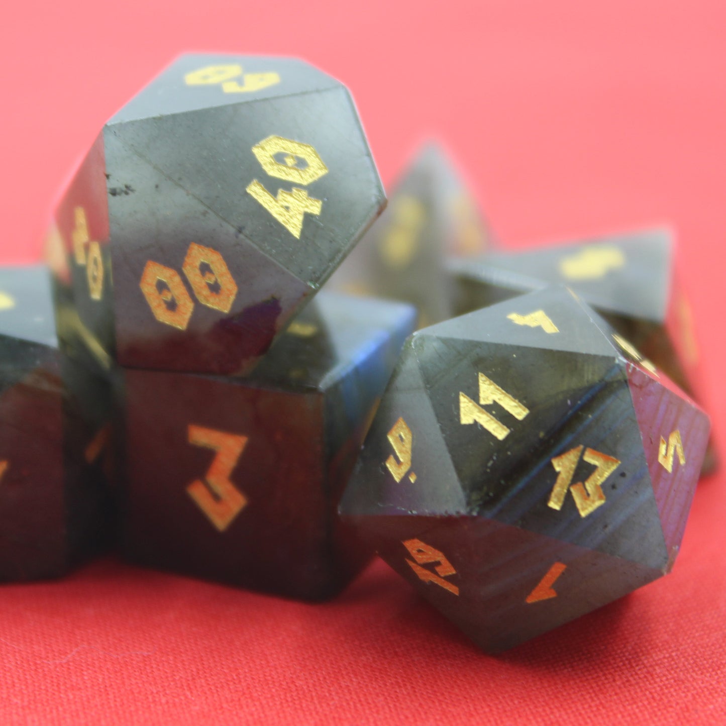 Close up of Labradorite dice set showcasing gold numbers and dark stone dice on a coral cloth.
