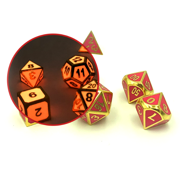 Imperial Glow in the Dark pink dice scattered on a white background. The dice have pink faces with gold numbers and framing. There is a circle inset in the image, showing a portion of the image in darkness so that the glow in the dark effect can be compared to the dice in the light. In the dark, the dice glow a lighter pink color, and the gold numbers and framing look dark, almost black.