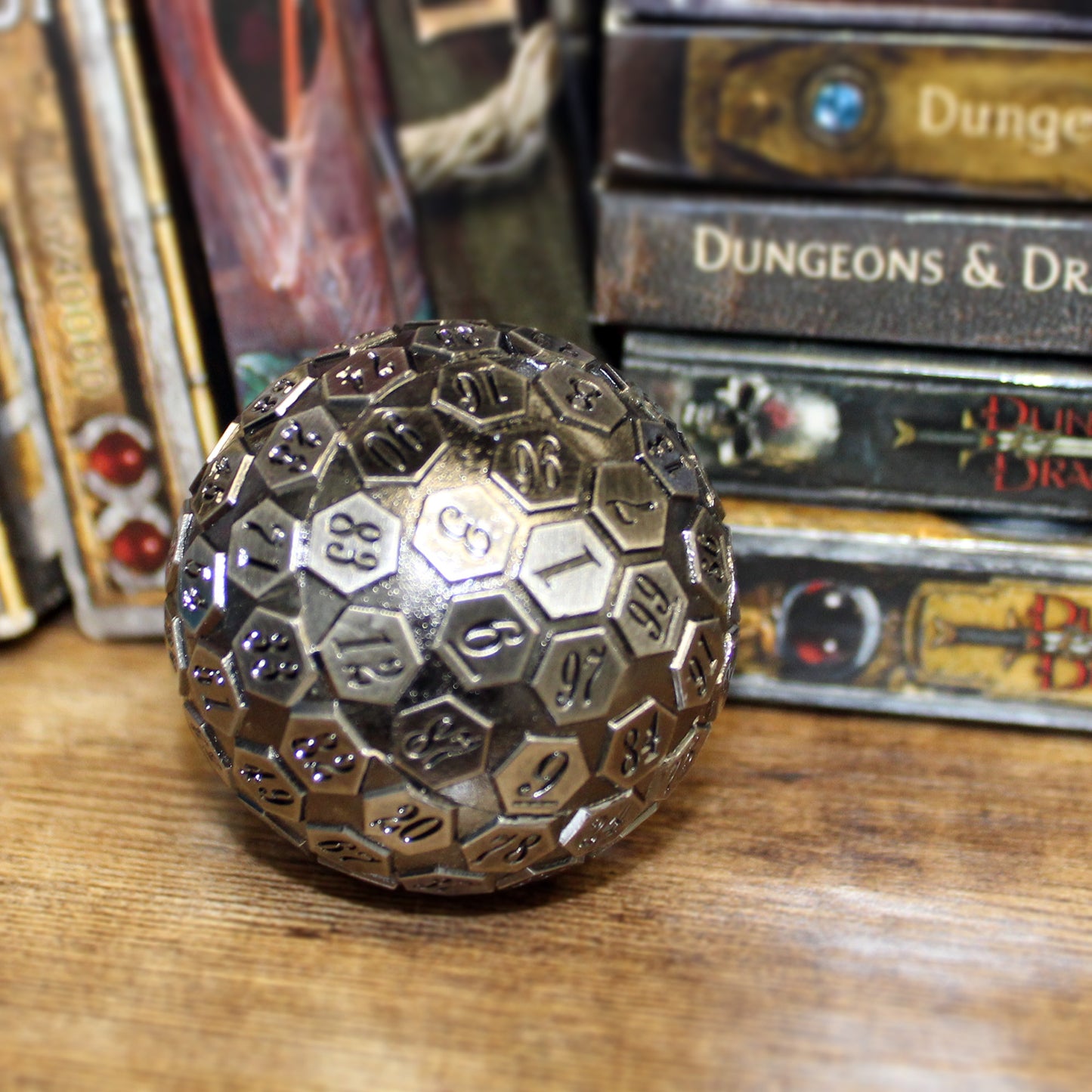 Metal D100 Antique Silver die on a wooden surface with DnD books behind it