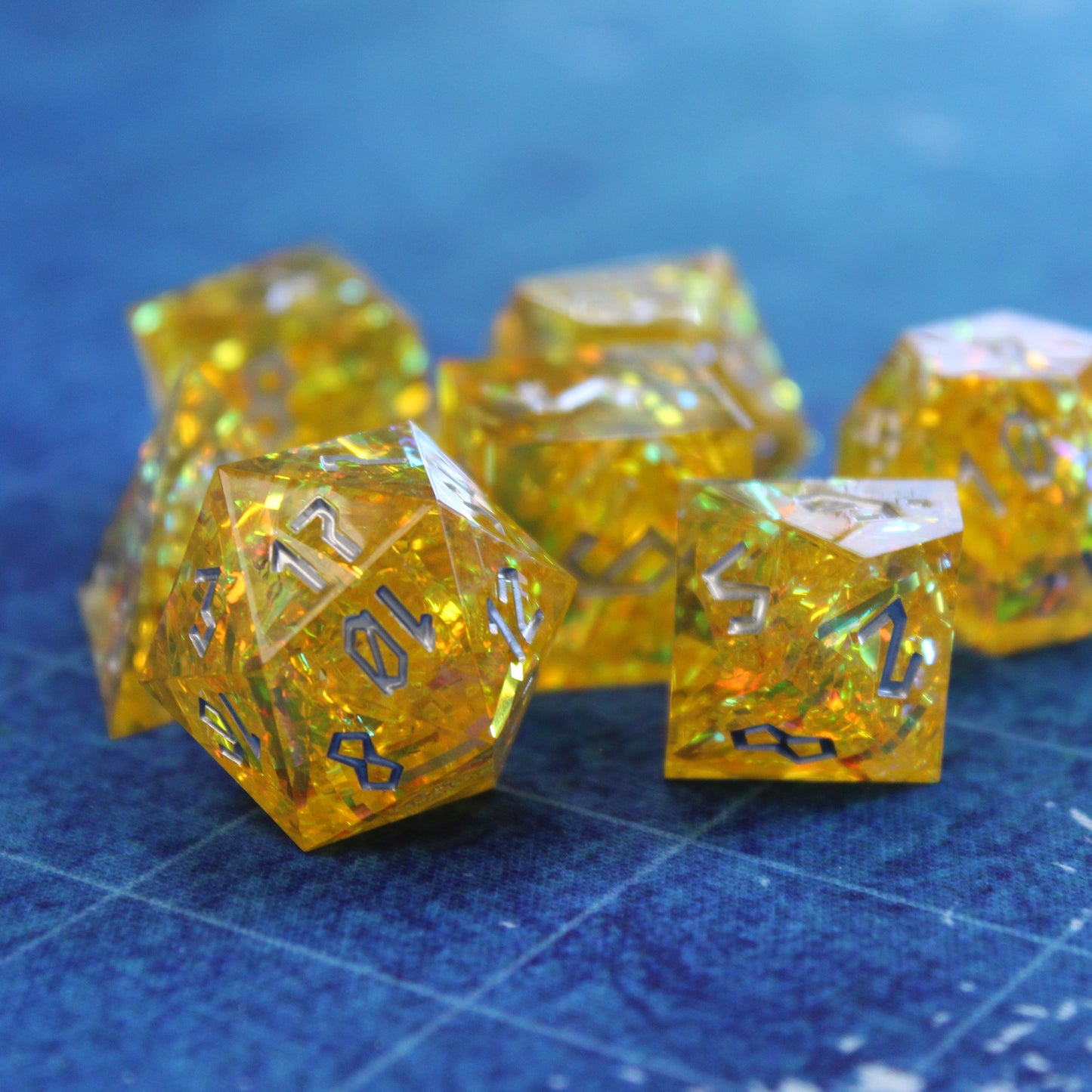 Full StarGlow Yellow sharp edge resin dice set displayed on a D&D grid, with translucent yellow resin and shimmering yellow and gold highlights.