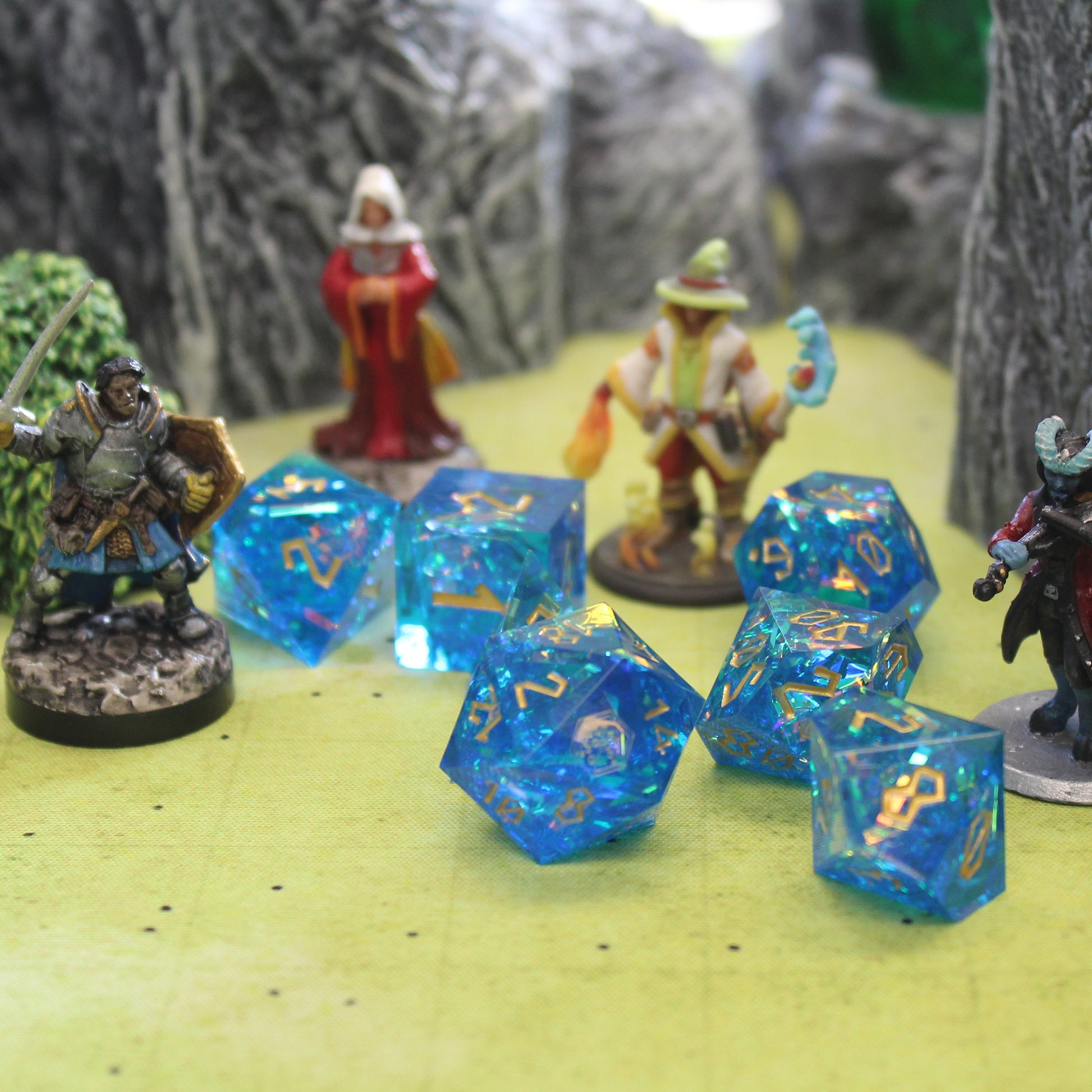 StarGlow blue dice scattered on a green game mat with four mini figures spaced out behind them, all surrounded by gray rocky wall set pieces.