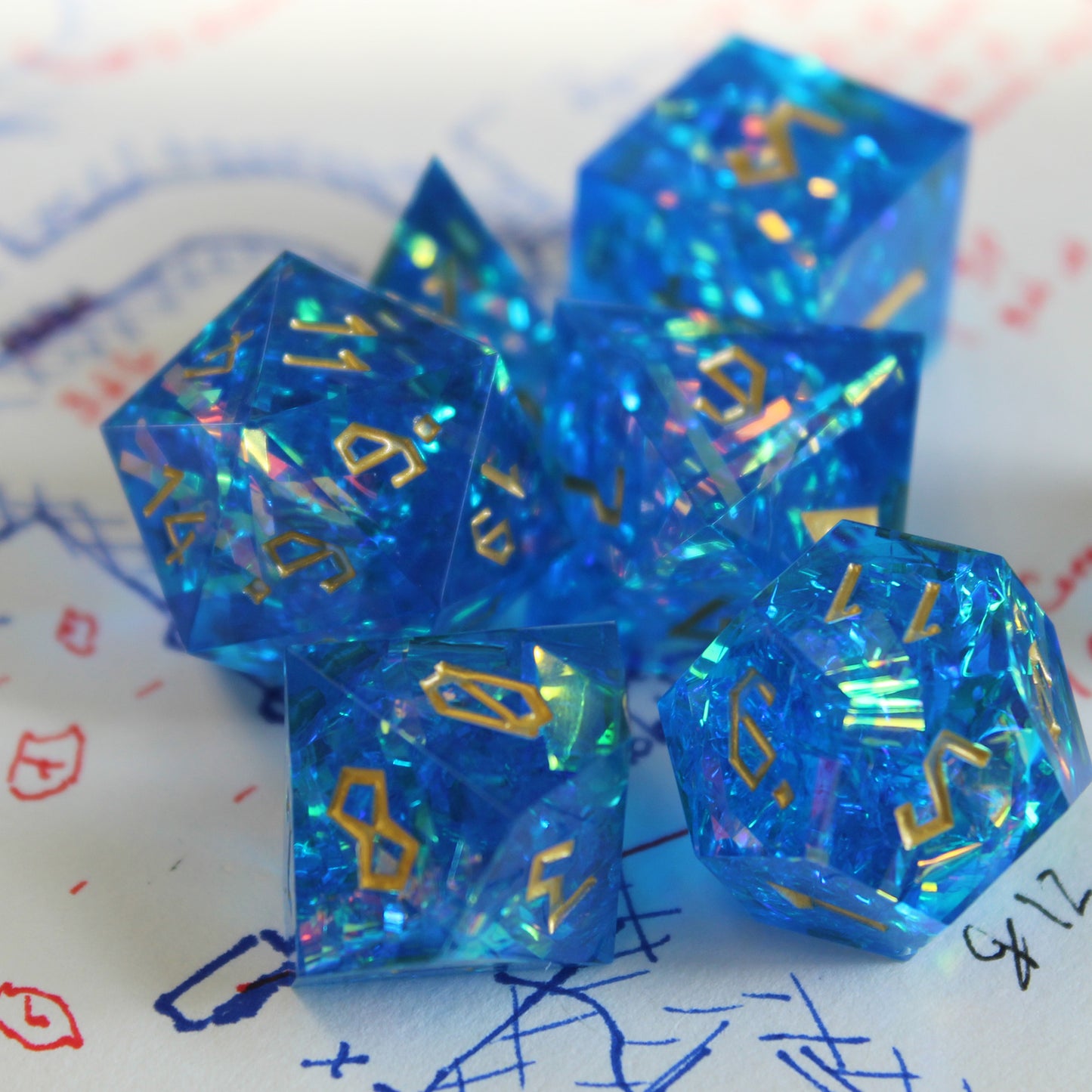 Blue StarGlow dice set arranged in a pile on top of a white piece of paper with red, black and blue pen ink doodles.