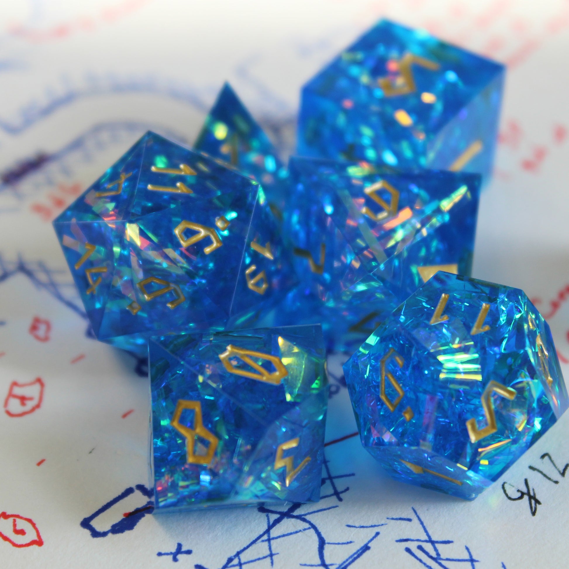 Blue StarGlow dice set arranged in a pile on top of a white piece of paper with red, black and blue pen ink doodles.