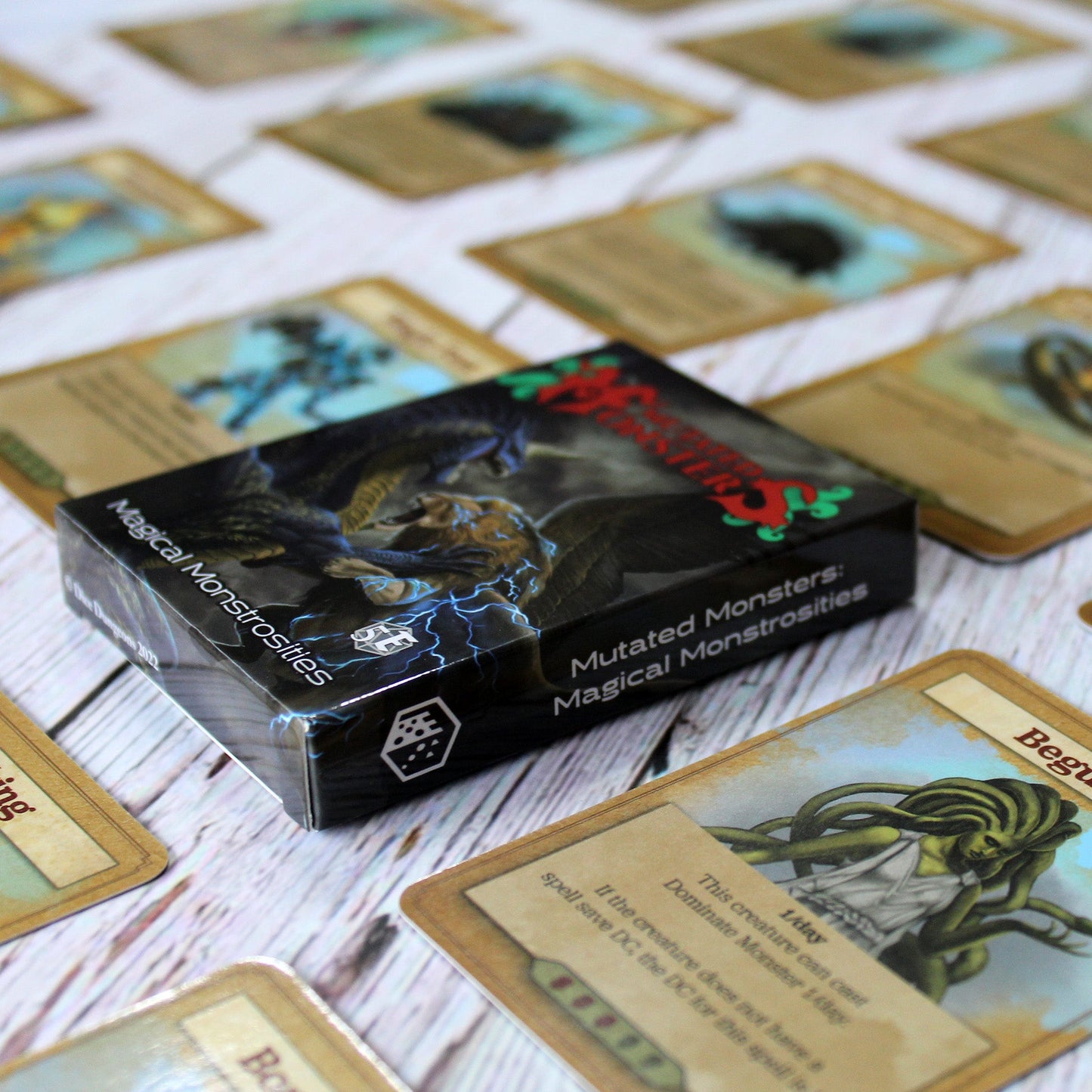 Deck box in the center of the image with individual cards from the deck spaced out equidistant from each other in a repeating pattern, all on a white wood paneled background.