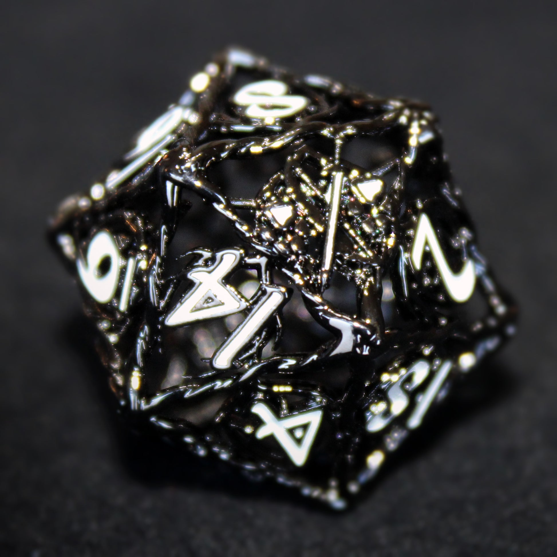 Close up of black Ranger dice on a gray background. Image showcases shiny black cage design and white number inking.