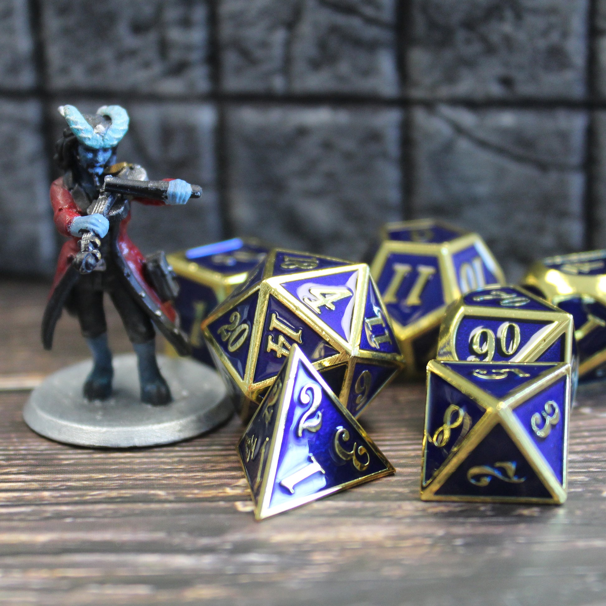 Imperial blue and gold dice set scattered on a wooden surface. Next to them is a mini figure for scale, and behind them is a stone set piece.