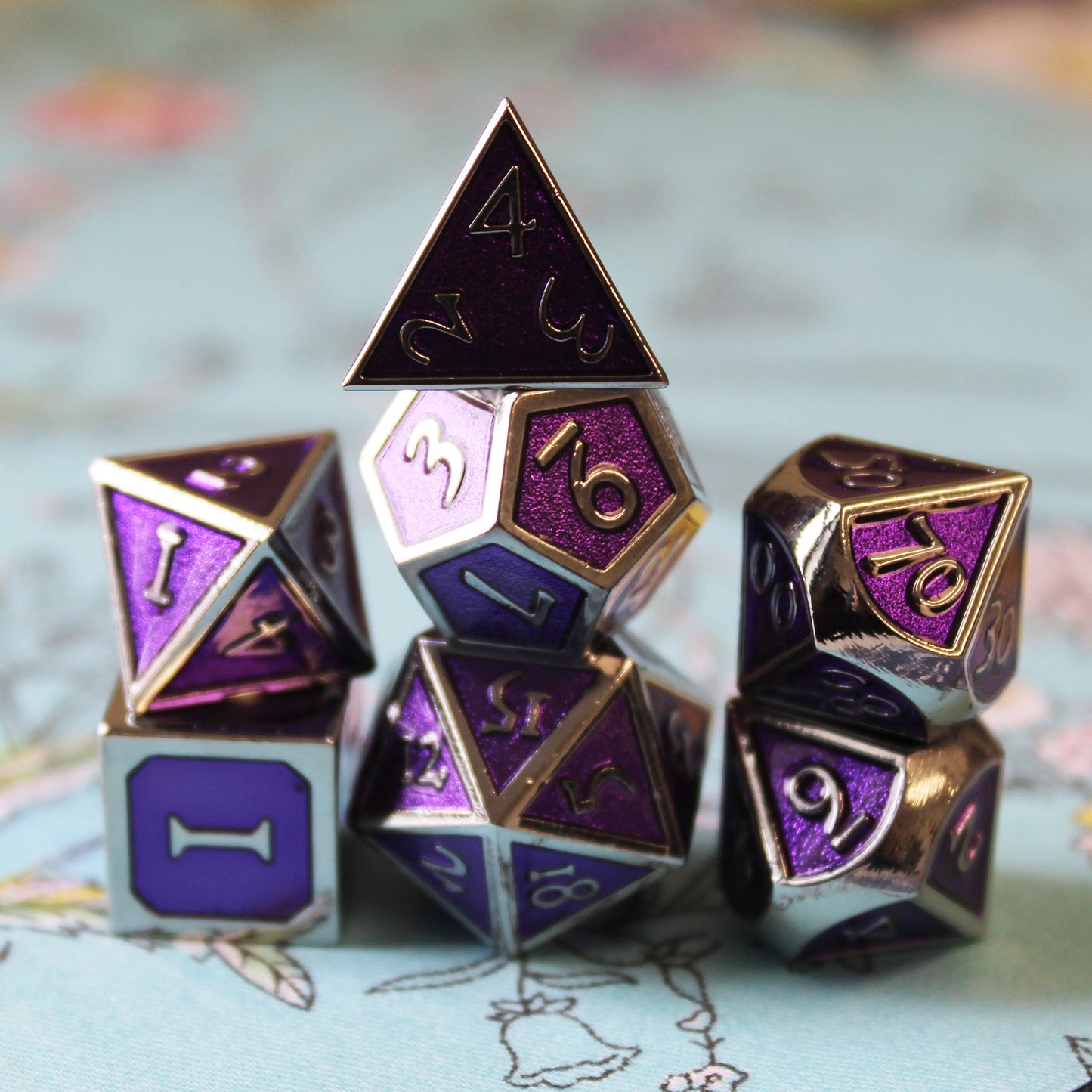 Imperial Magi Purple dice set placed in three stacks on top of a light green fabric with floral patterns.