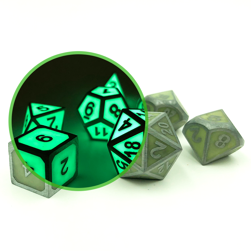 Imperial Glow in the Dark pink dice scattered on a white background. The dice have green faces with green numbers and framing. There is a circle inset in the image, showing a portion of the image in darkness so that the glow in the dark effect can be compared to the dice in the light. In the dark, the dice glow bright green, and the green numbers and framing look black.