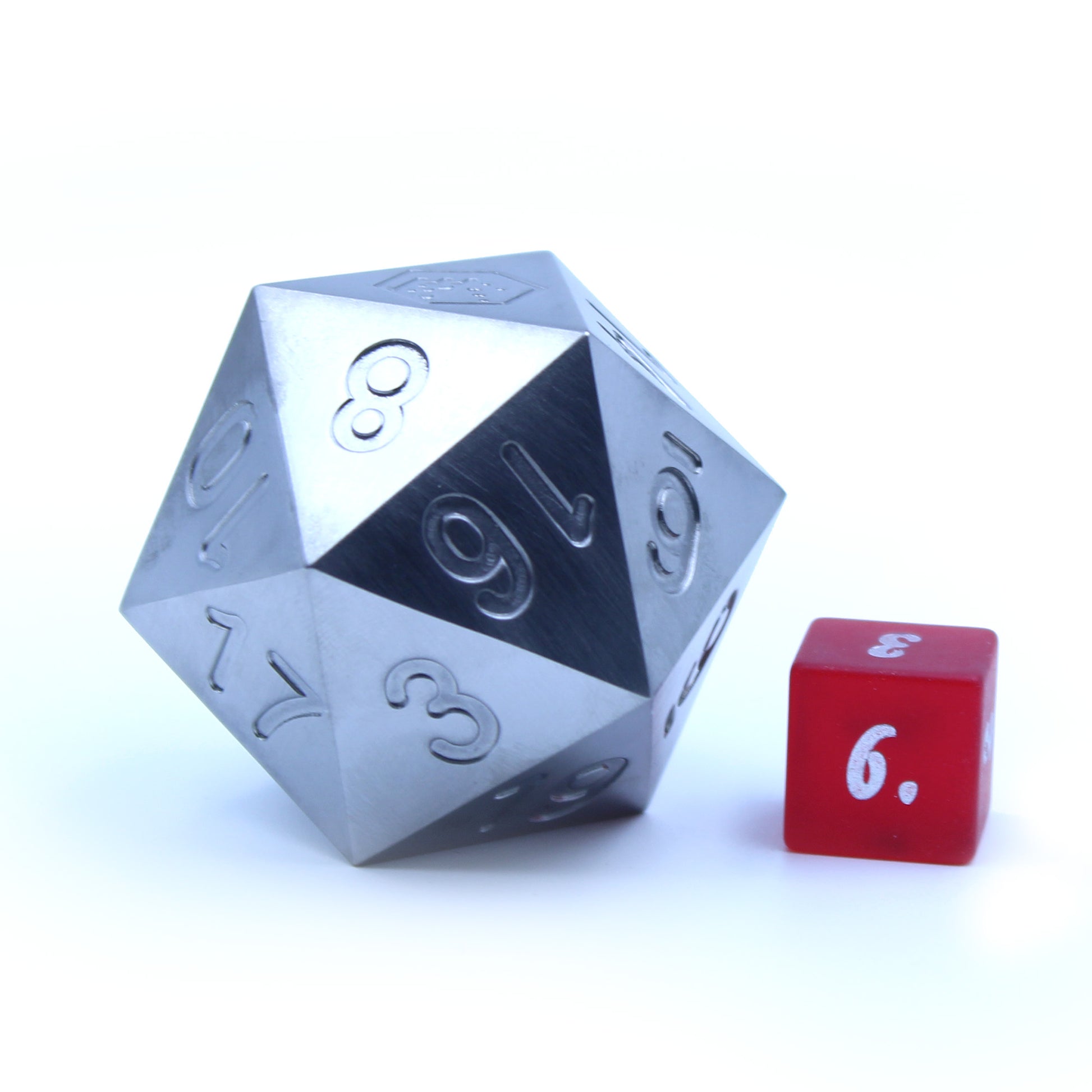 An oversized silver-colored metal twenty-sided die sitting next to a regular-sized red six-sided die.