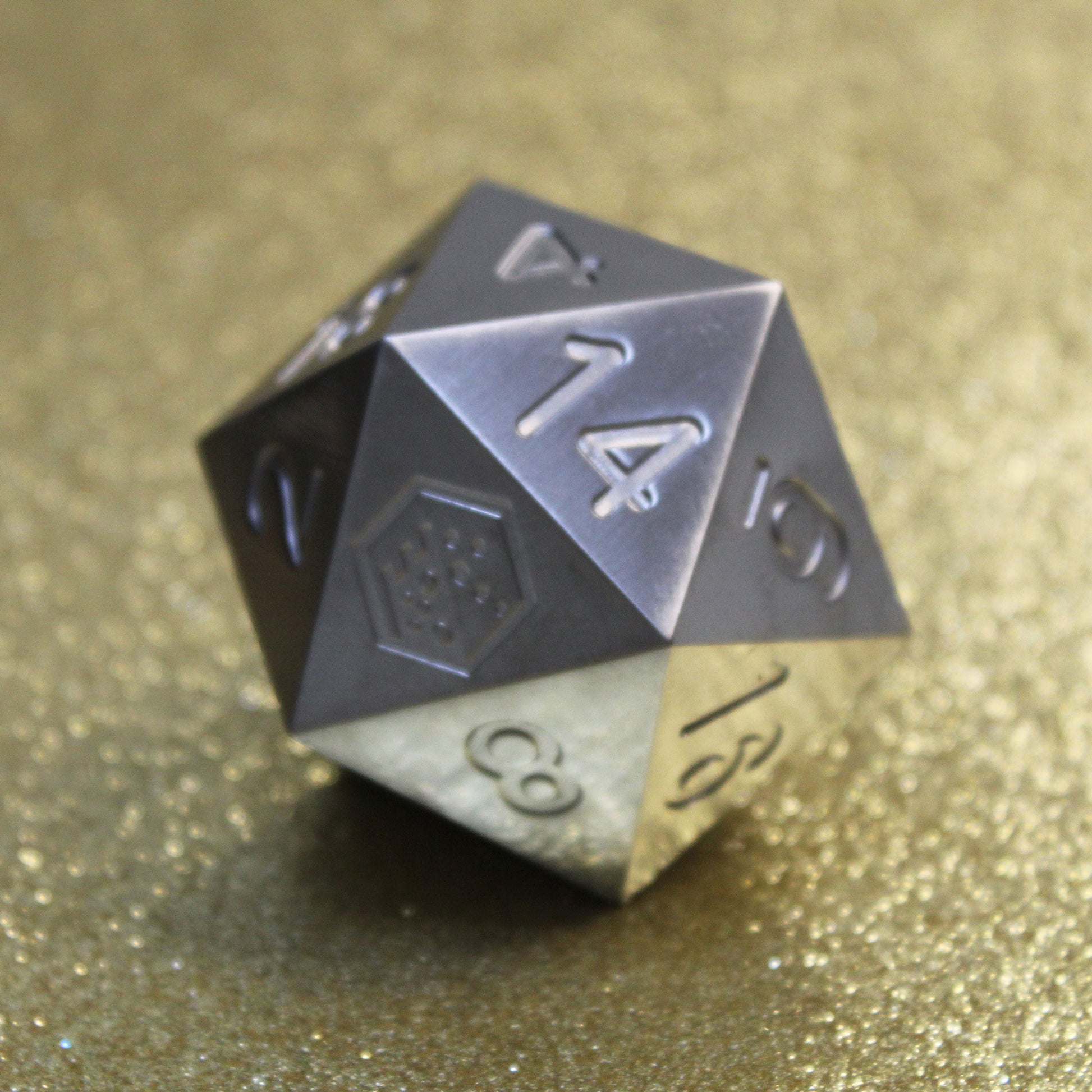 An oversized silver-colored metal twenty-sided die with a Dice Dungeons logo in place of the number twenty sitting on a glittery gold background.