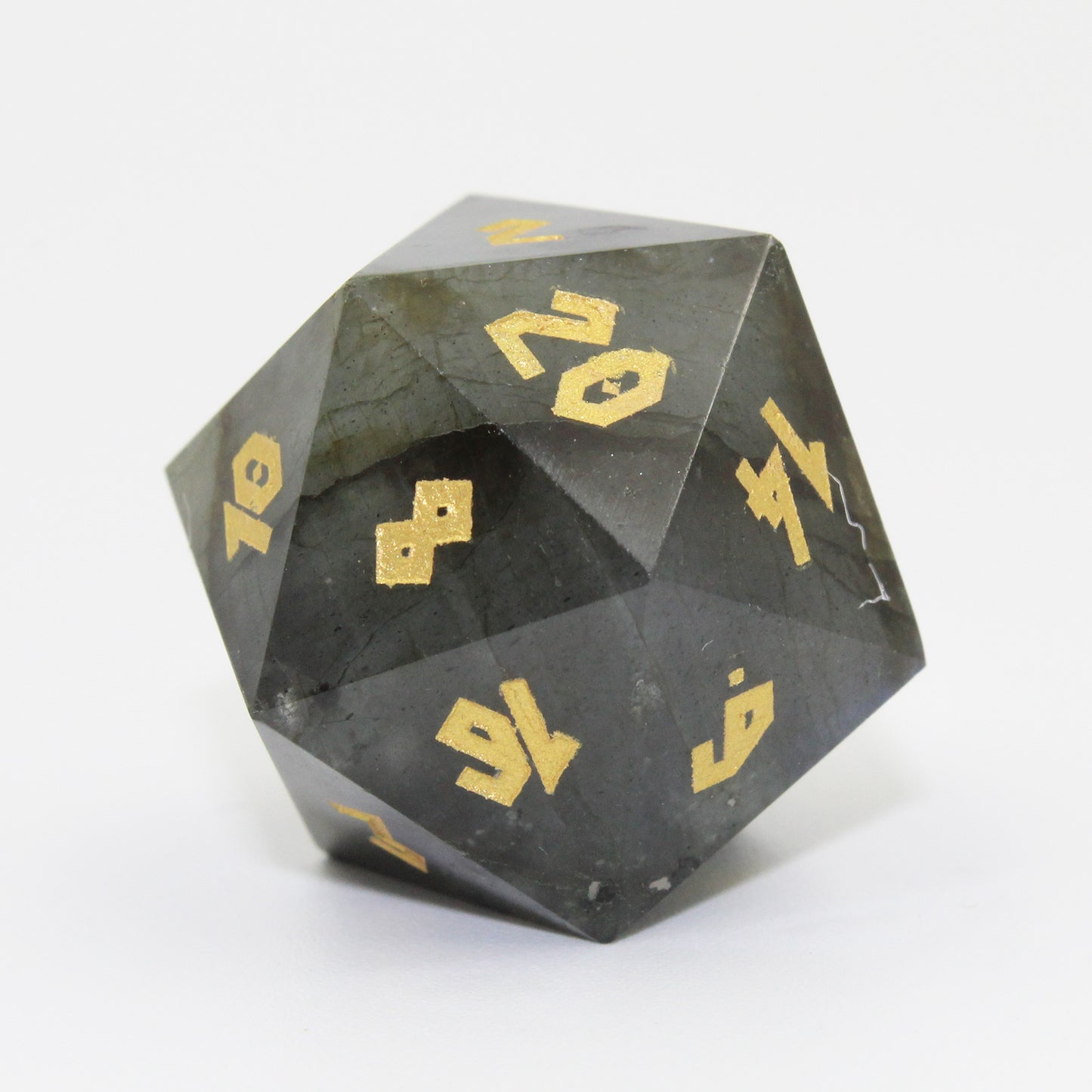 A closeup of D20 Labradorite die on a white background. The natural banding of the stone.