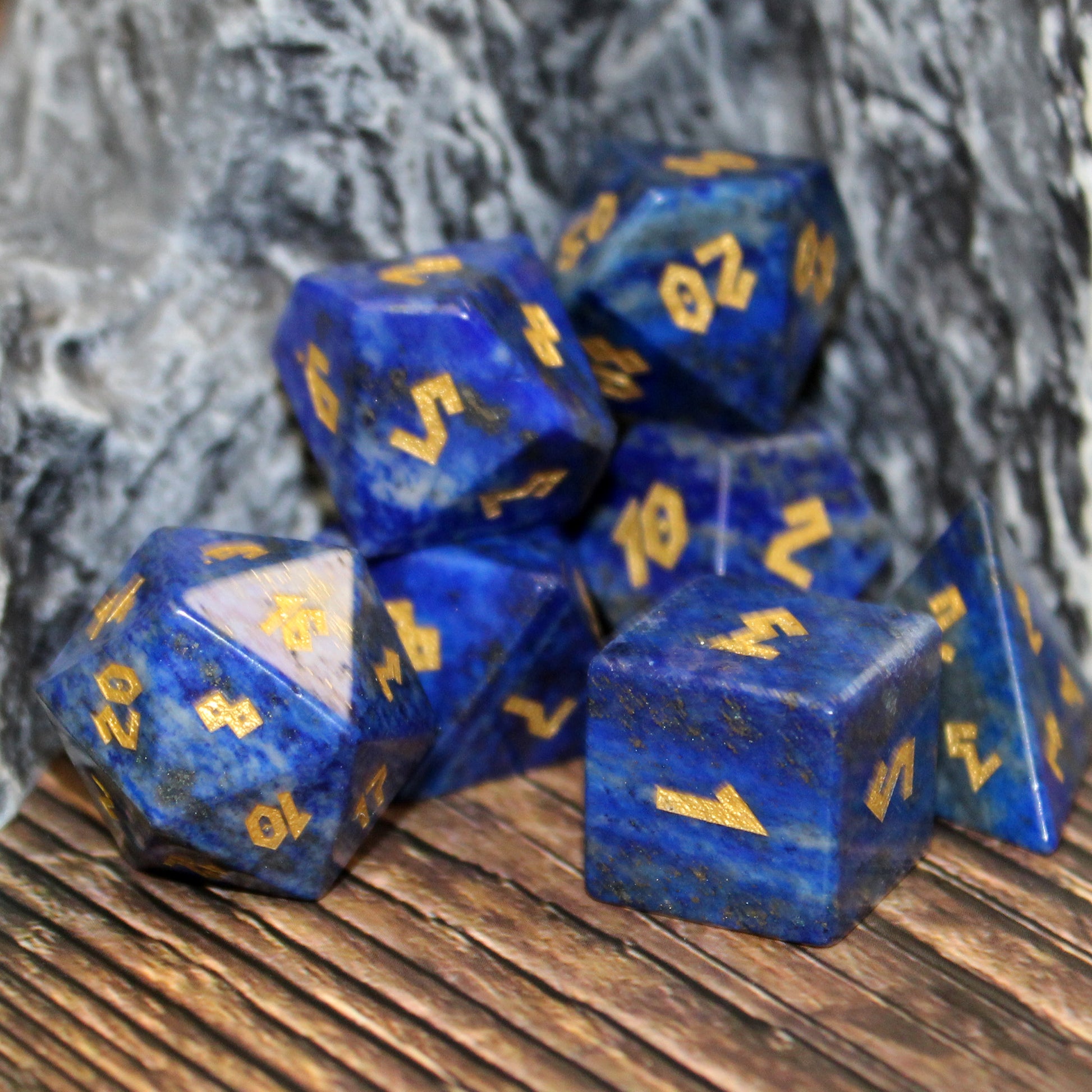Lapis Lazuli dice set scattered on a wooden surface, with a rocky set piece behind them