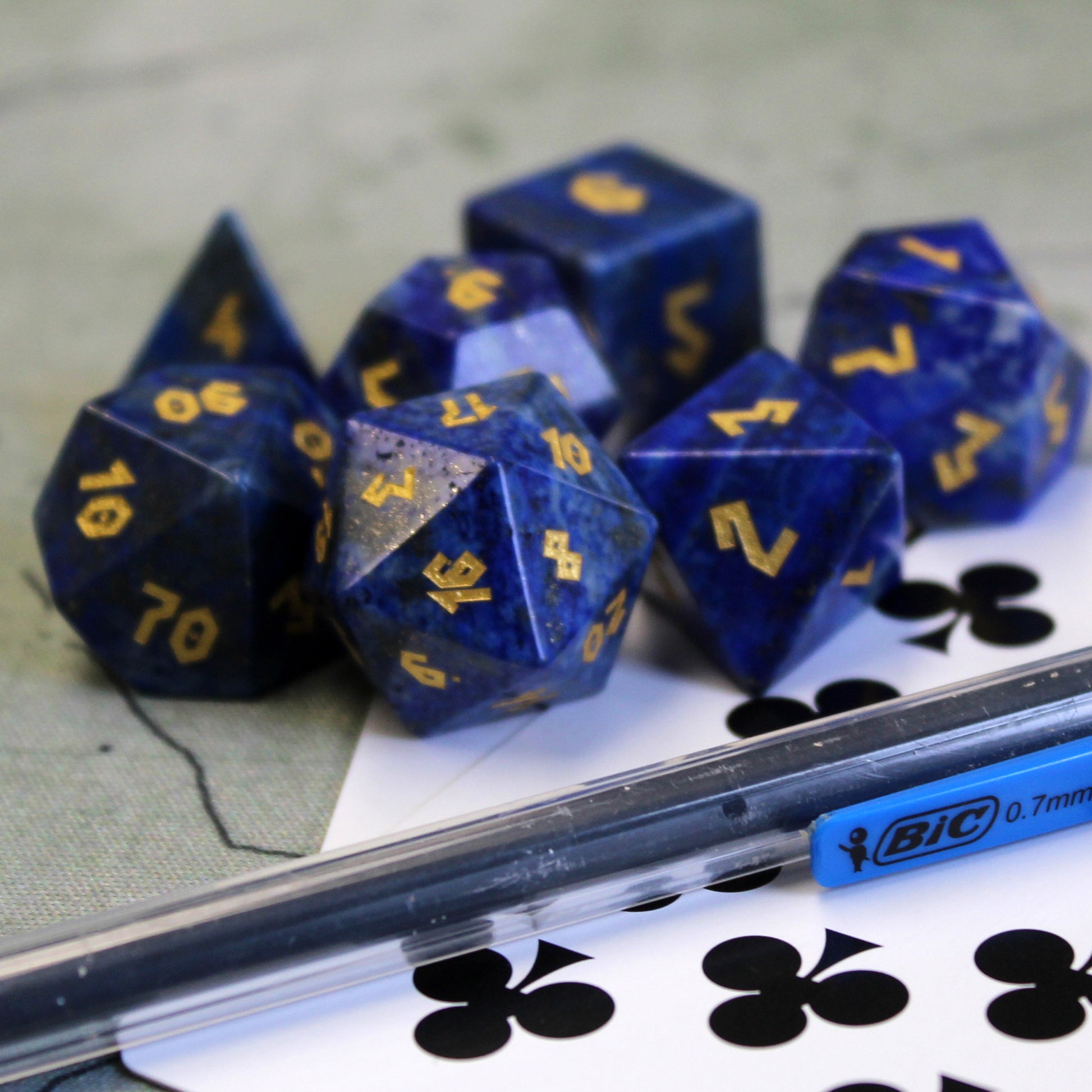 Lapis Lazuli dice set scattered on top of a green play mat, with a playing card and a mechanical pencil position in front