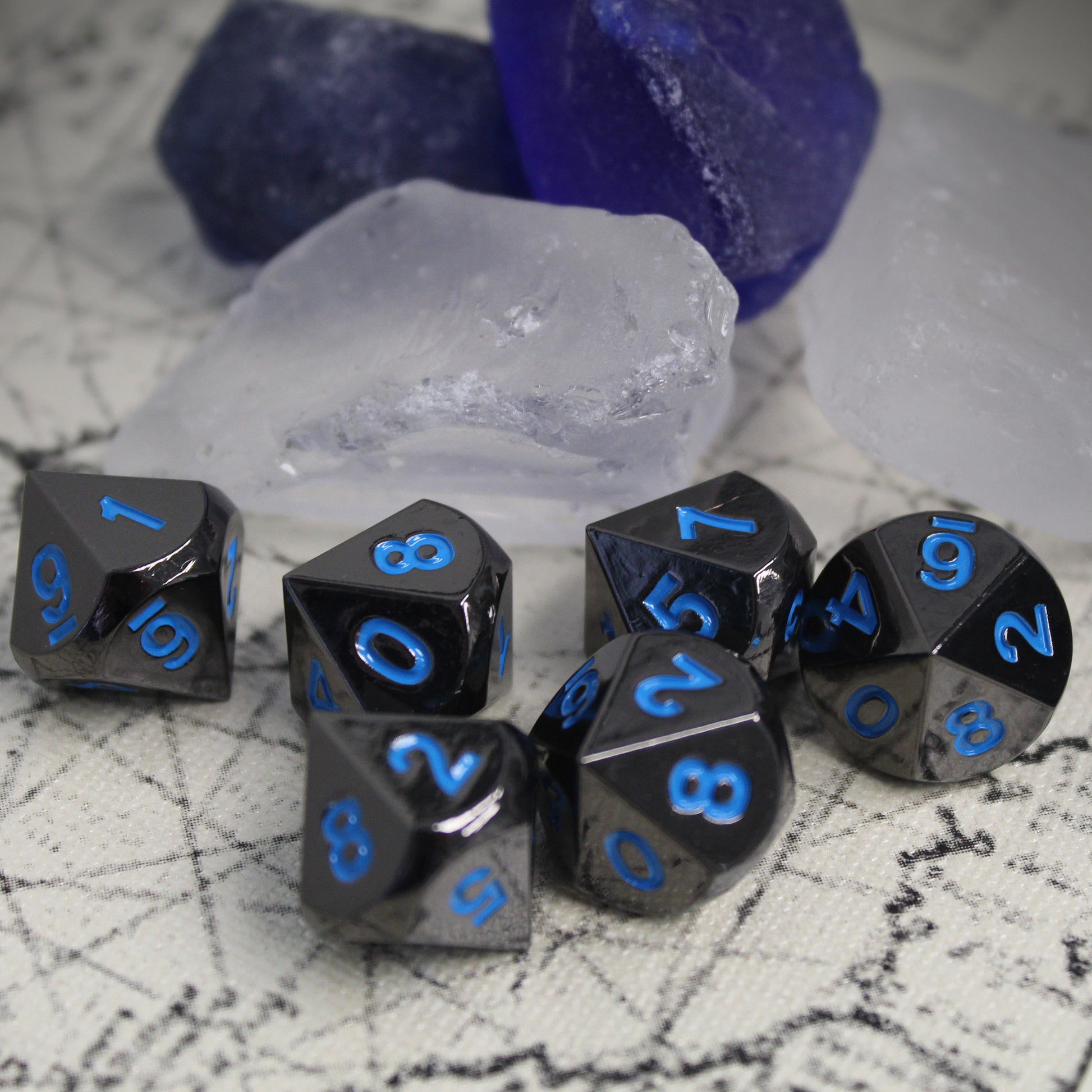 Metal Black Frost dice set scattered on a play mat in front of clear and blue rocks.