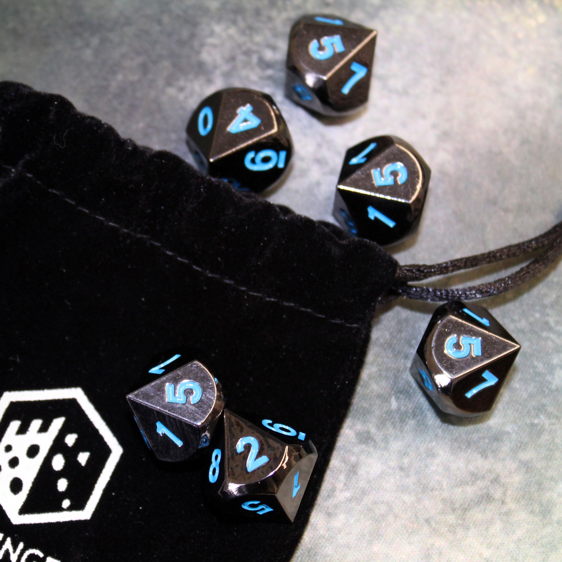 Metal Black Frost dice set scattered on top of a Dice Dungeons dice bag and light colored gray fabric.