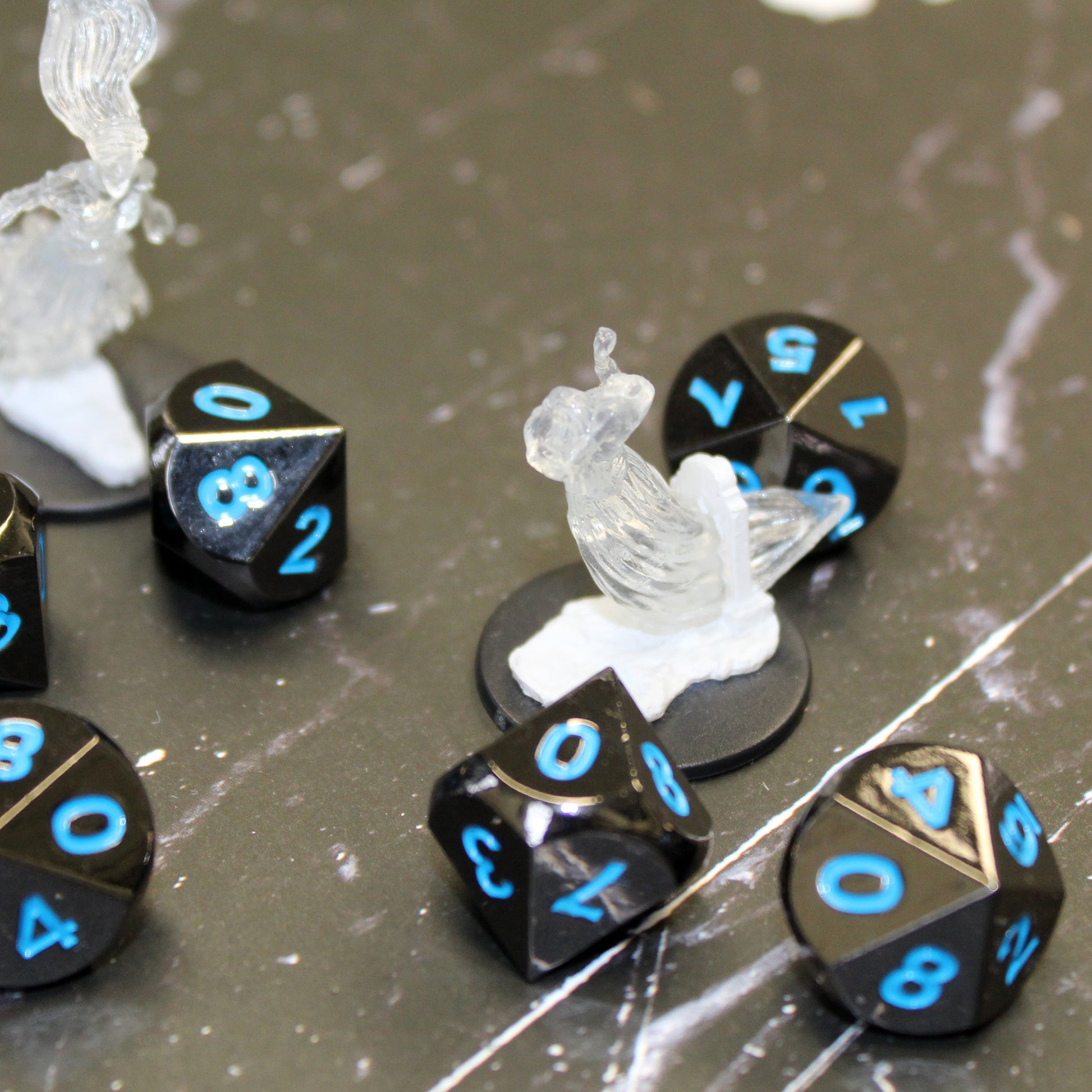 Metal Black Frost dice set scattered on a black and white marble surface with two clear mini figures.