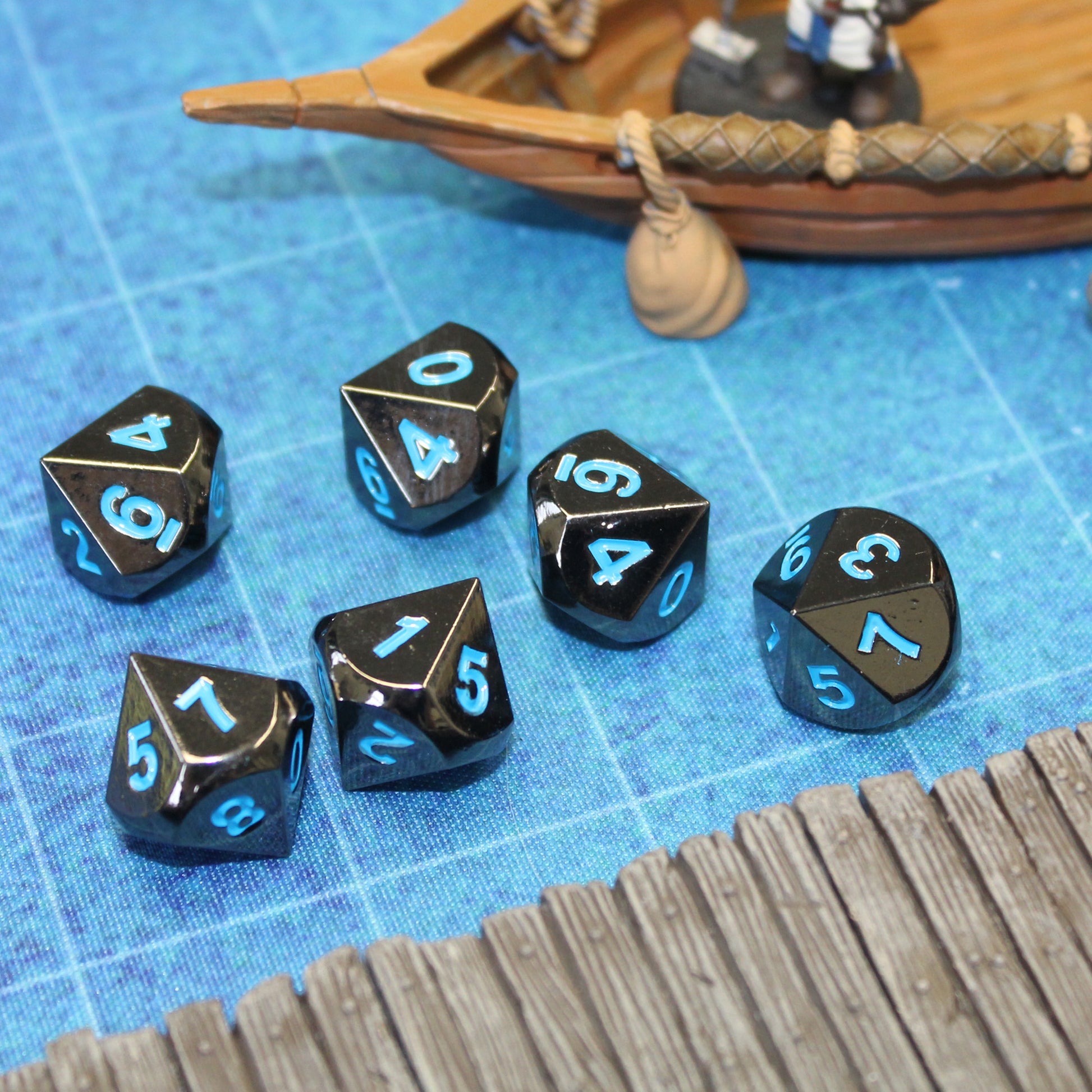 Metal Black Frost dice set on top of a blue game mat, with a pier set piece in front and a boat set piece in the background.