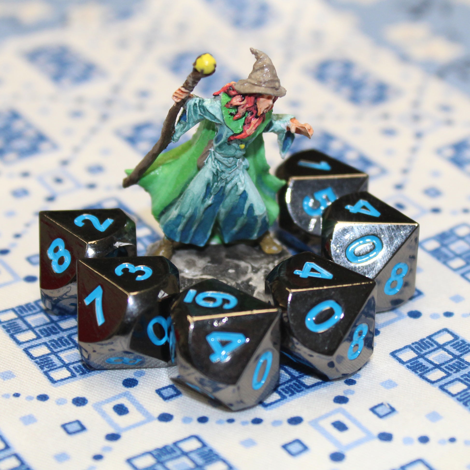 Metal Black Frost dice set surrounding a mini figure in a semi-circle on top of a white and blue patterned fabric.
