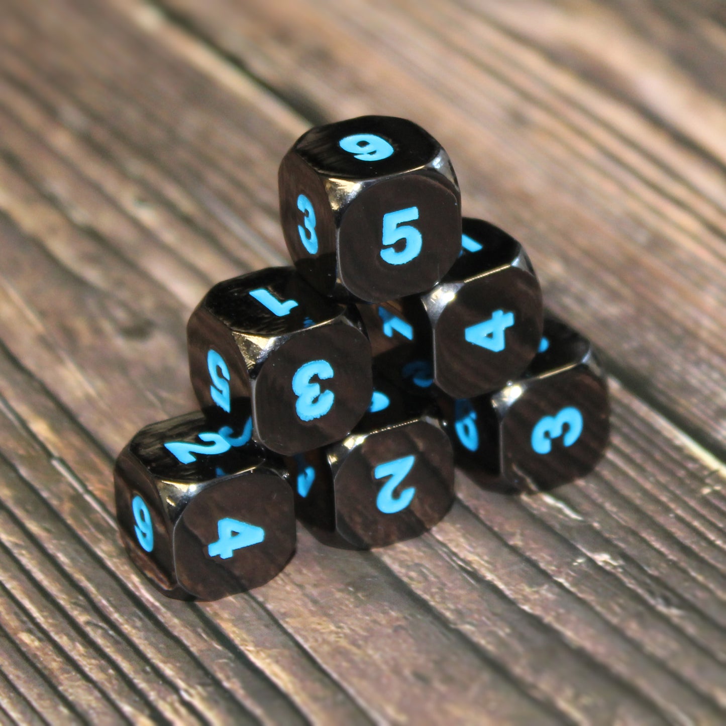 Six Black Frost D6 stacked in a pyramid on a wooden surface